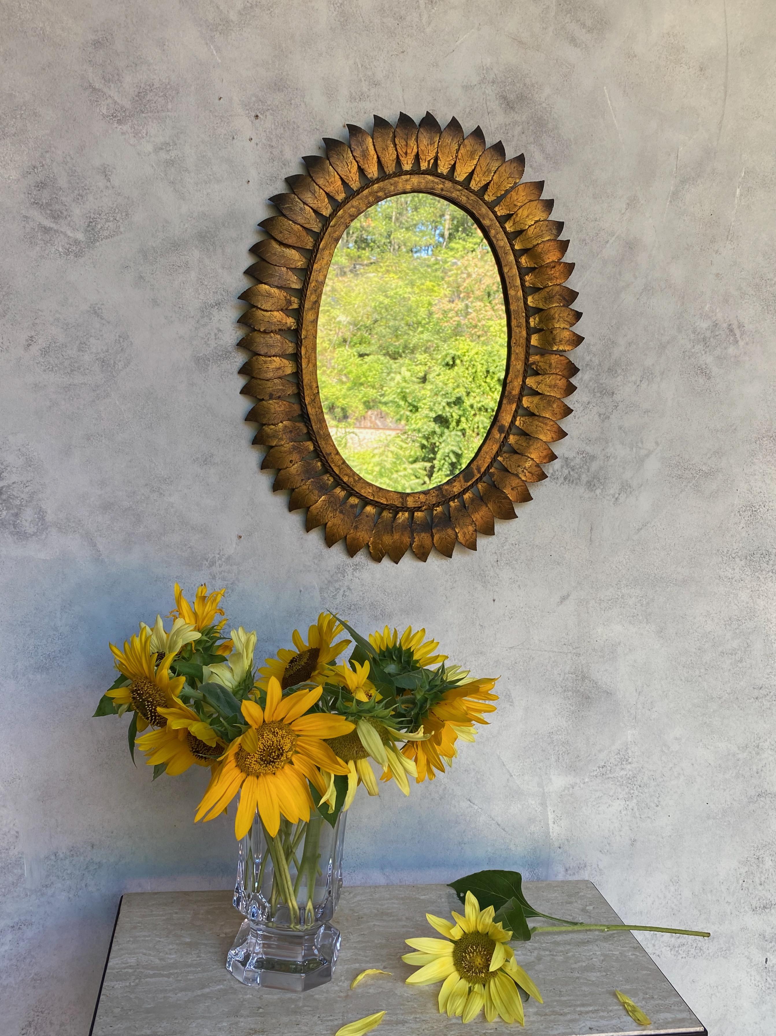 Spanish 1950s oval sunburst mirror in gilt iron and metal frame. Thin overlapping leaves are attached to a braided rope decorative border surrounding a hammered gilt frame. We recently added a felt backing to the mirror to give it more protection