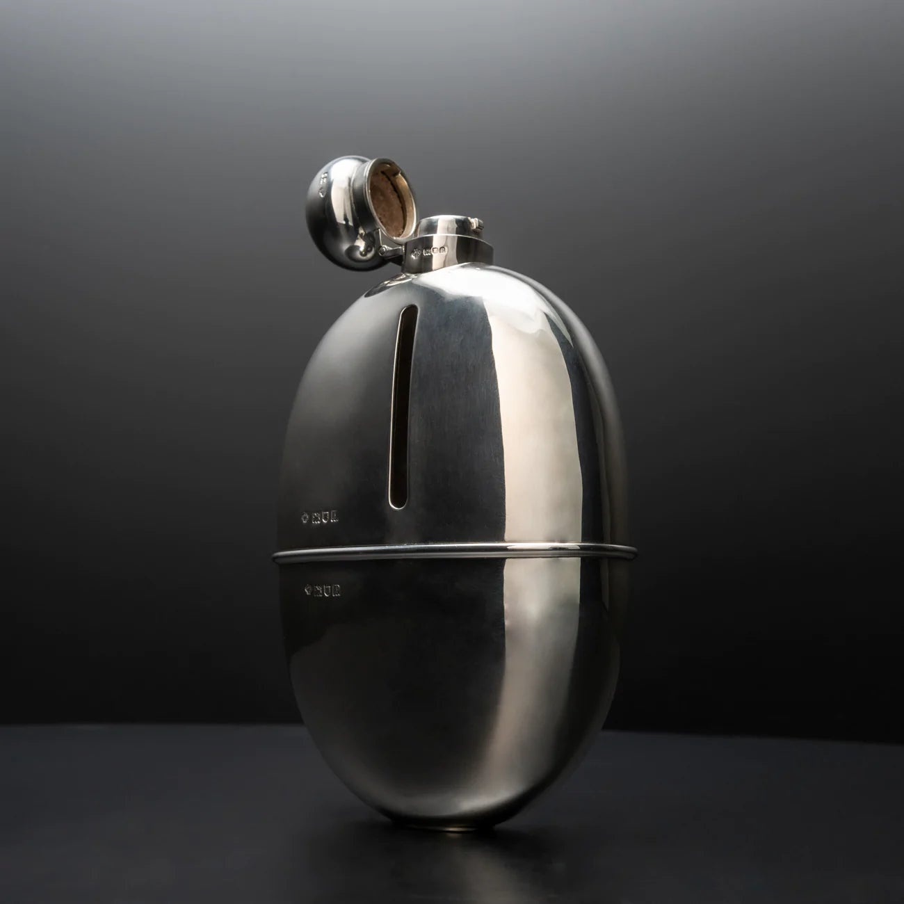 Large shaped silver and glass flask, hallmarked London 1910. The body of the flask is topped with a cork lined stopper that is on a hinged bayonet closer. A silver removable cup covers the lower half of the body and the silver covering the top half