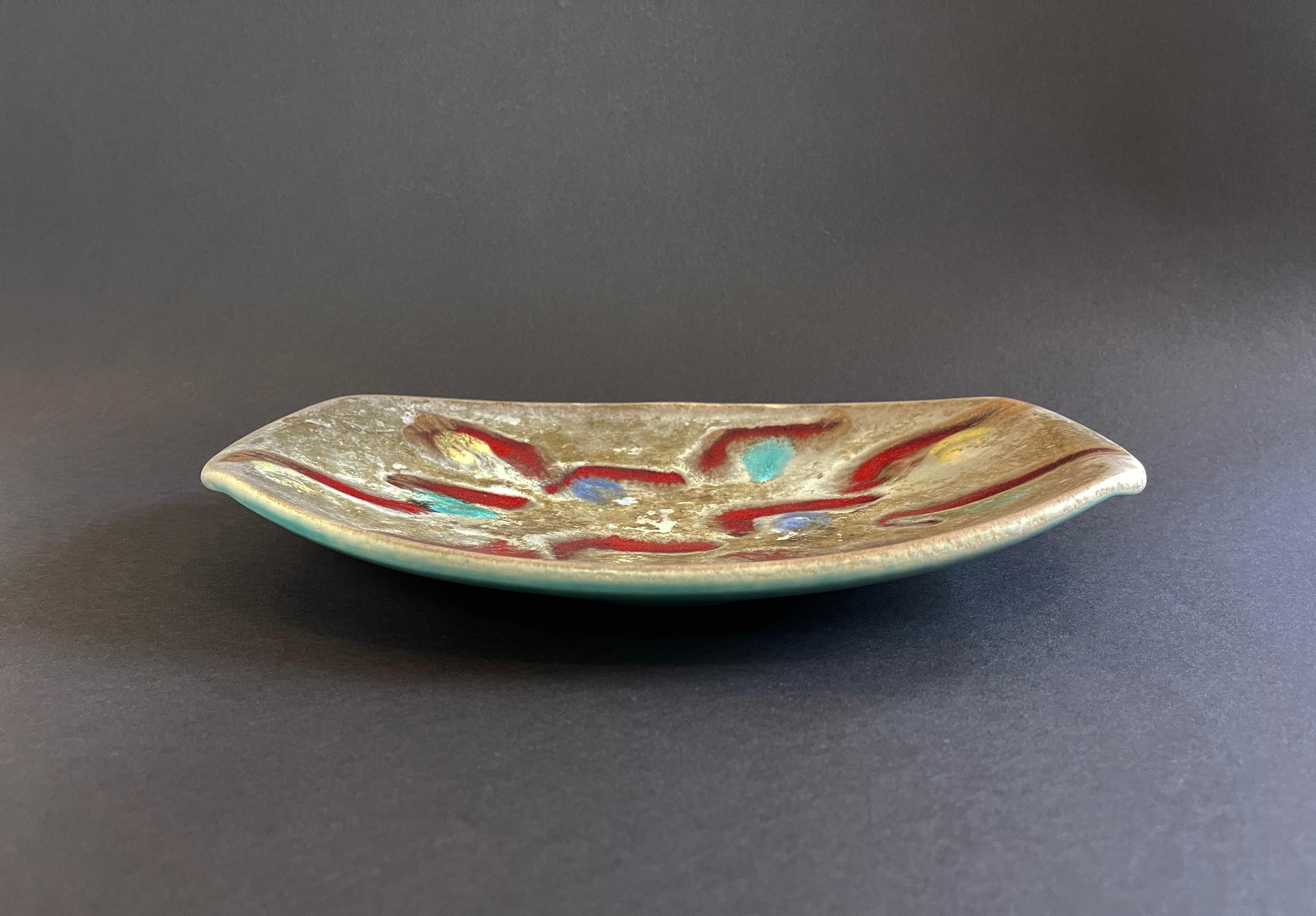 Un'opera d'arte insolita è questa ciotola o piatto da portata ovale e poco profonda di Jasba, realizzata in ceramica.
Lo splendido smalto decorativo è disponibile in una classica combinazione di colori della metà del secolo scorso: beige, rosso, blu