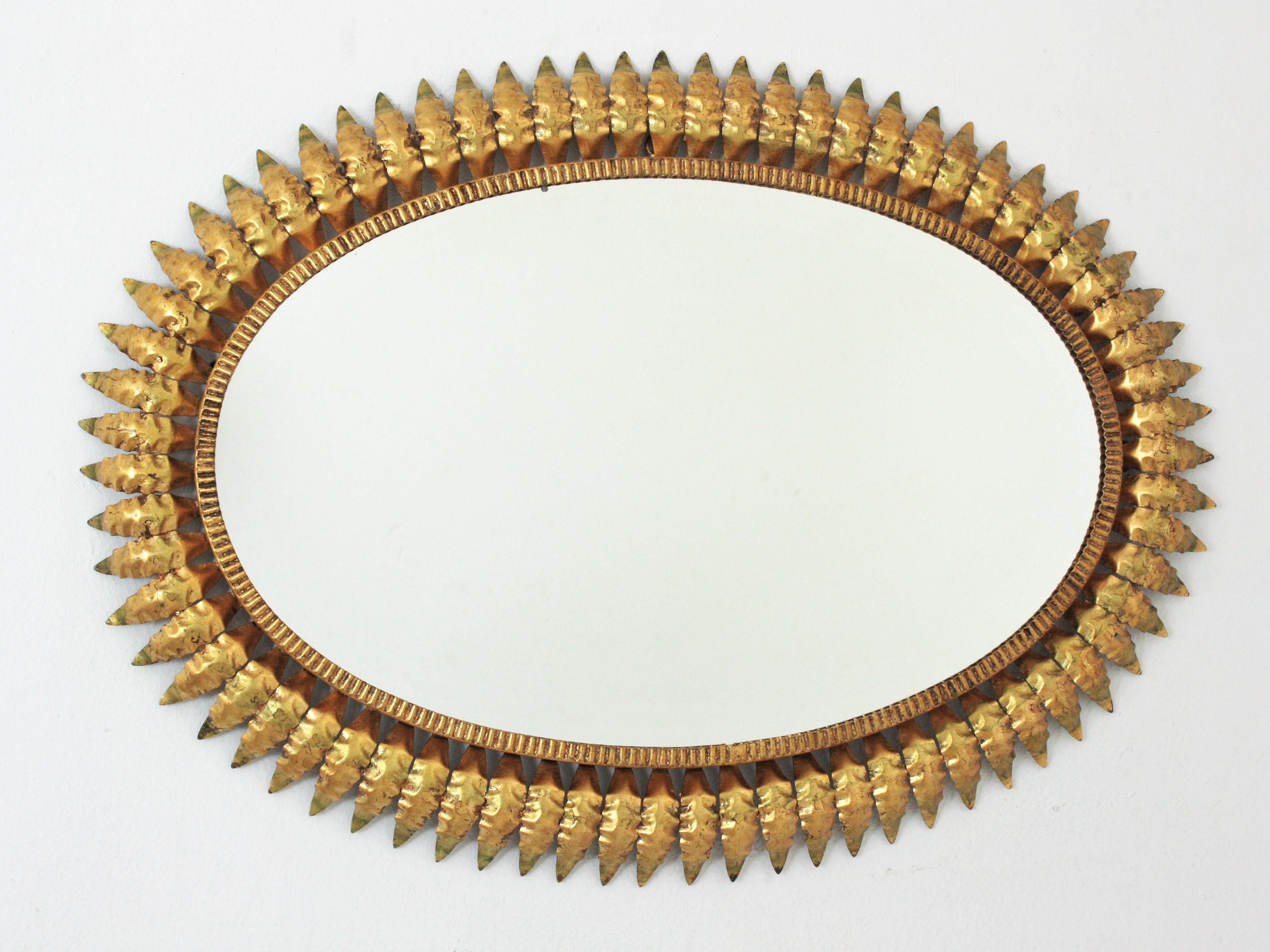 Mid-Century Modern hand-hammered iron sunburst oval wall mirror with gold leaf finish, Spain, 1950s.
This highly decorative leafed sunburst gilt iron mirror has a nice patina and gold leaf gilding and green accents.
A great choice placed in a