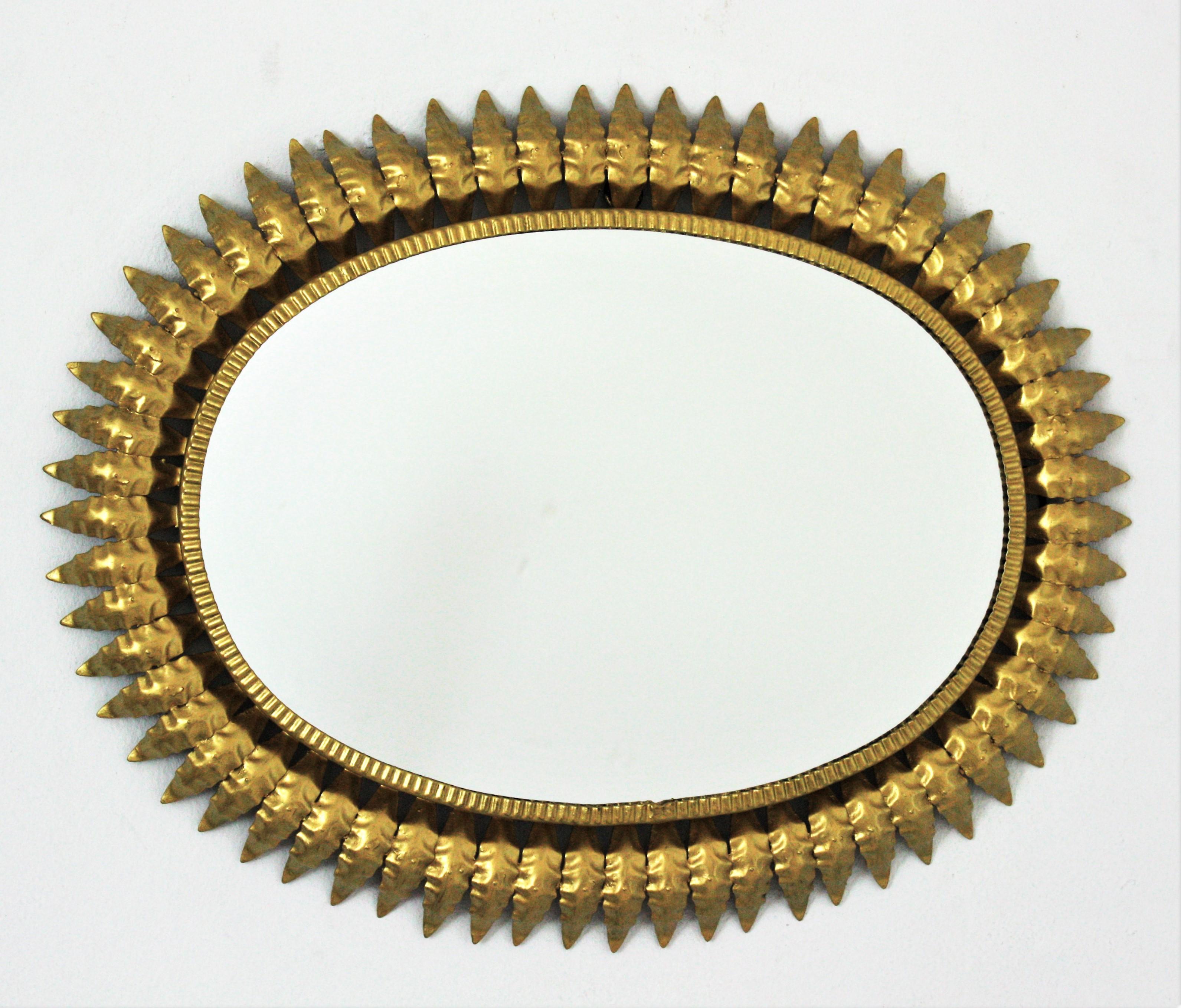 Mid-Century Modern gilt metal sunburst oval wall mirror, Spain, 1960s.
This highly decorative leafed sunburst gilt iron mirror has a nice color and an elegant construction. 
A great choice placed in a powder room, dressing room and over a console