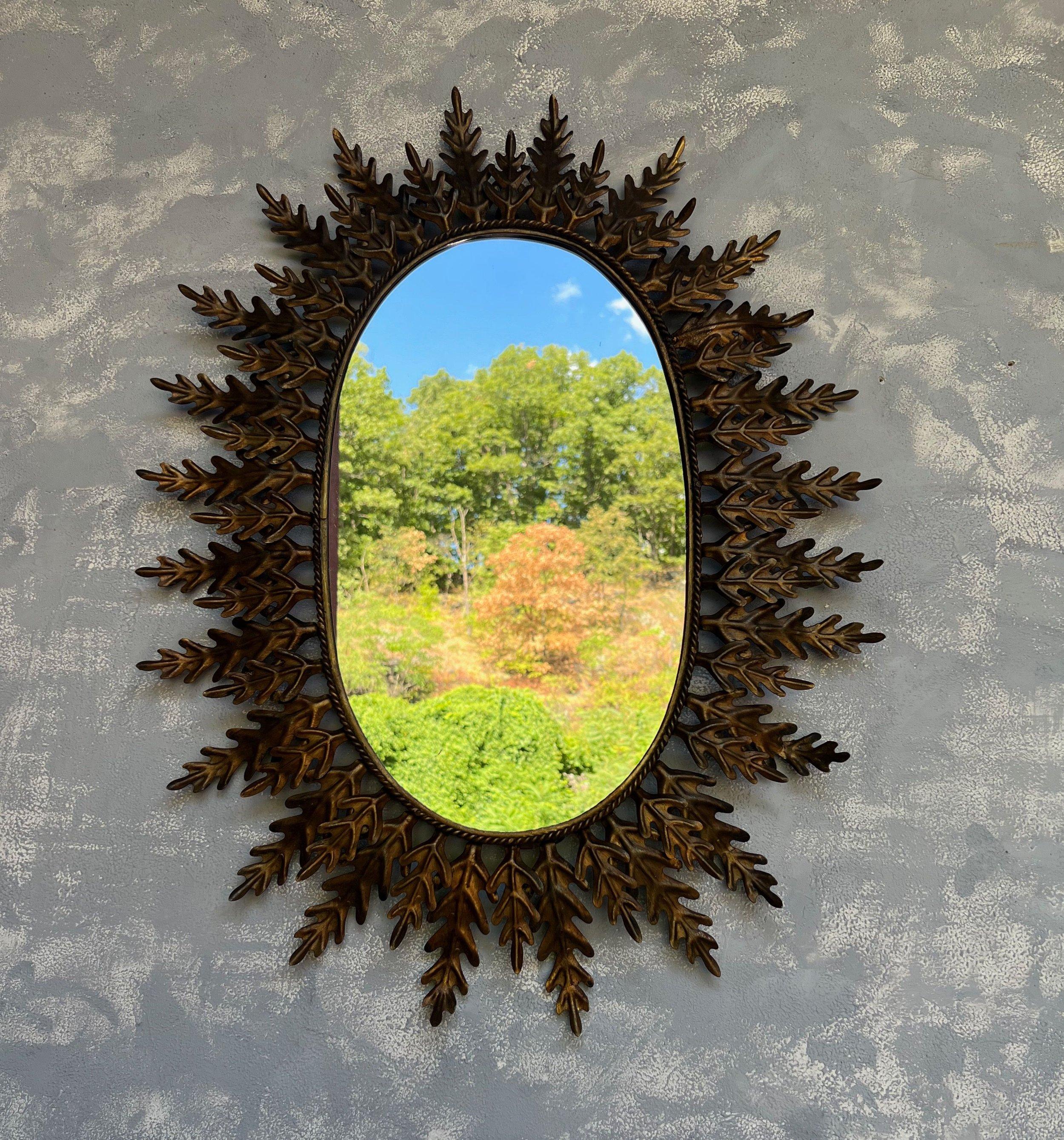This exceptional oval gilt metal sunburst mirror possesses an air of sophistication and elegance. Crafted in Spain during the 1950s, it features alternating large and small leaves or rays surrounding a delicately braided frame. The evenly spaced