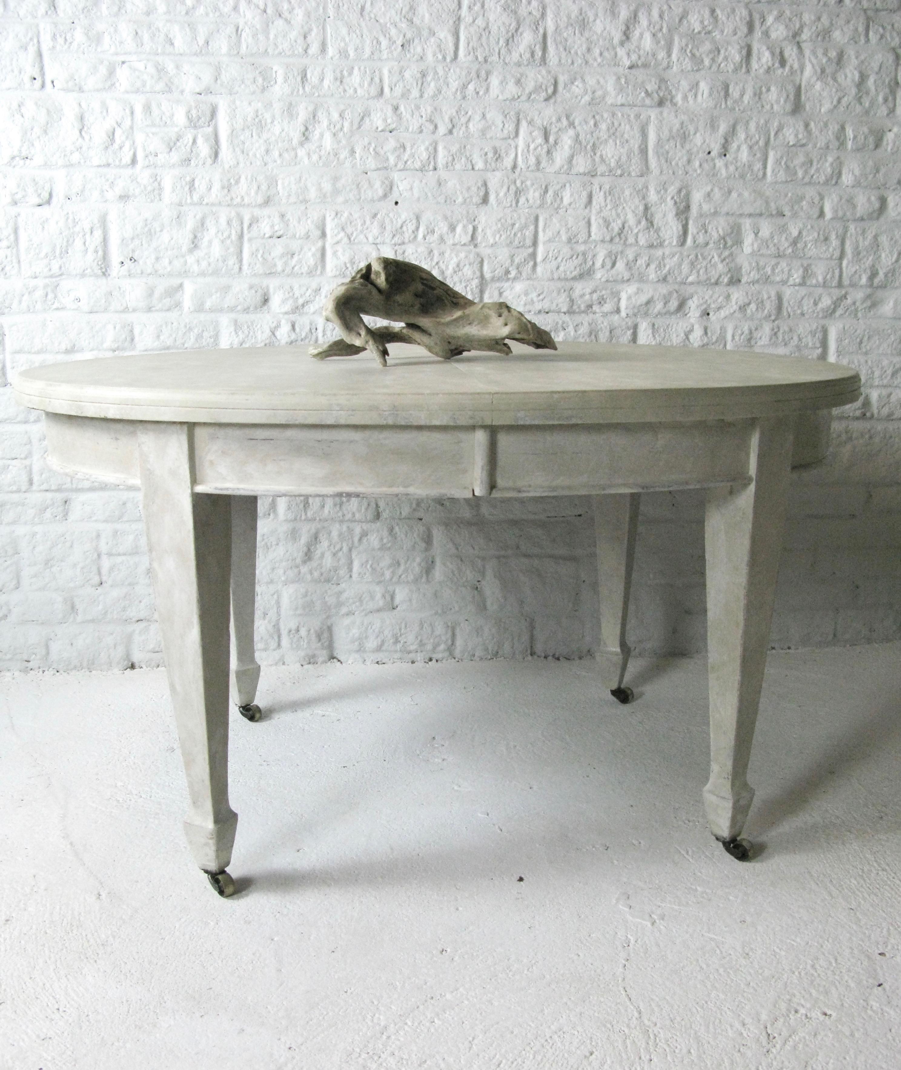 Gustavian style painted cream with a crème (ish) tint and a white border touches.

The table has robust tapered fluted legs and is extendable. Leave is not available. 

Supported on brass castors.
Excellent as a kitchen table.

Word from the