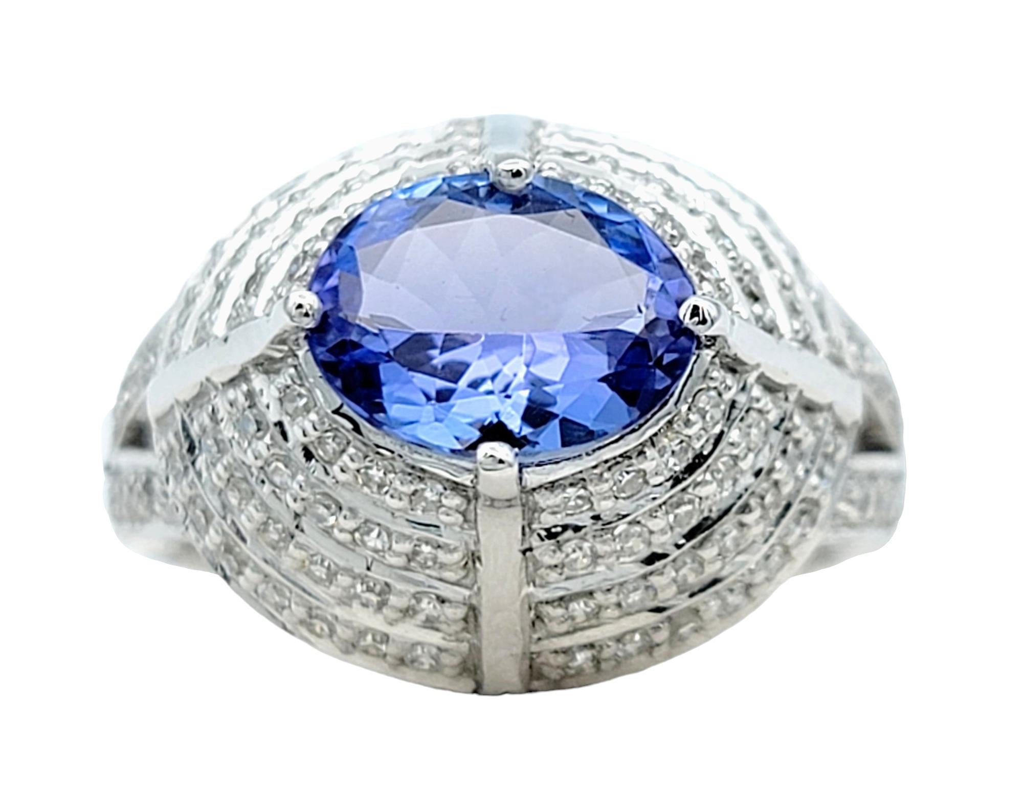 Ring Size: 7

This opulent dome ring is a true masterpiece set in radiant 18 karat white gold. At its focal point lies a captivating oval tanzanite, a gemstone known for its enchanting violet-blue hue. Surrounding the tanzanite, graduated rows of