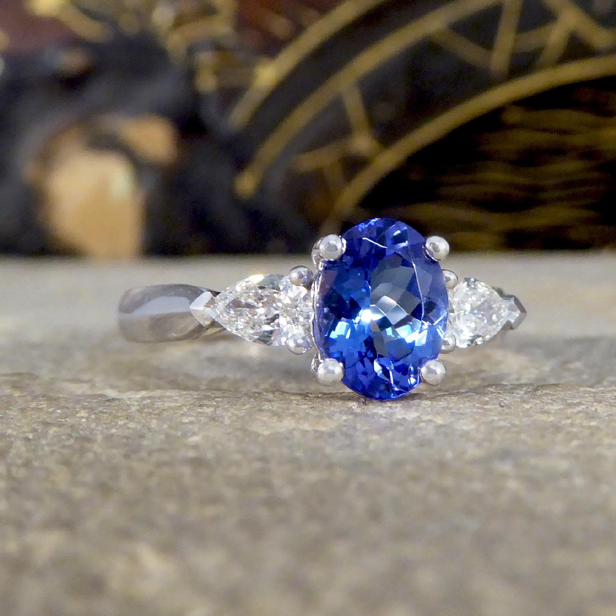 This Oval Cut Tanzanite and Pear Cut Diamond three stone ring in Platinum is a masterpiece of elegance and refinement. At its centre, the ring features a captivating oval tanzanite, renowned for its deep, mesmerising blue-violet hue that symbolises