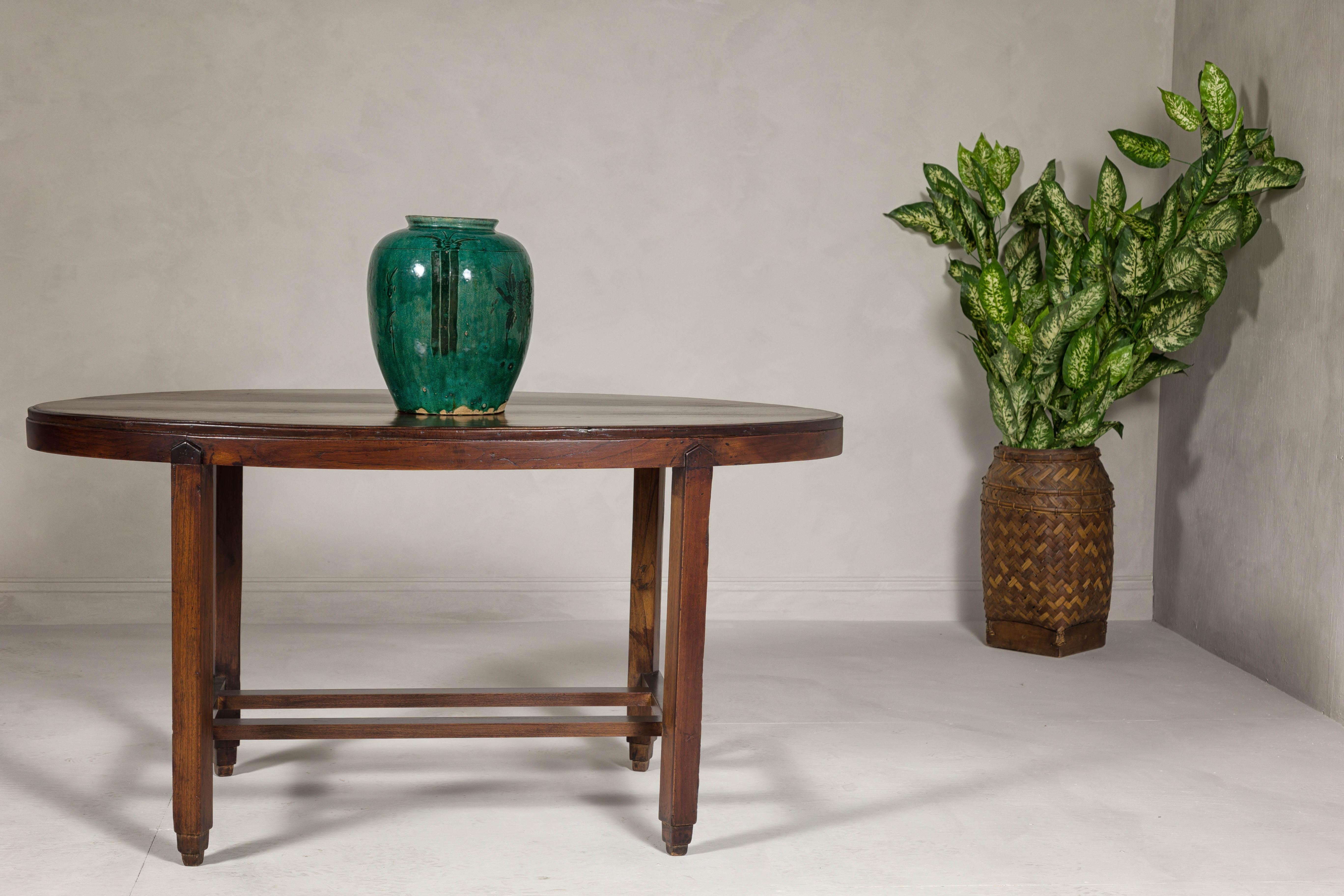A vintage oval top center table with inverted stepped pyramid feet and double H-Form cross stretcher. This vintage center table boasts an elegant oval top and a distinctive base design featuring inverted stepped pyramid feet connected by a double