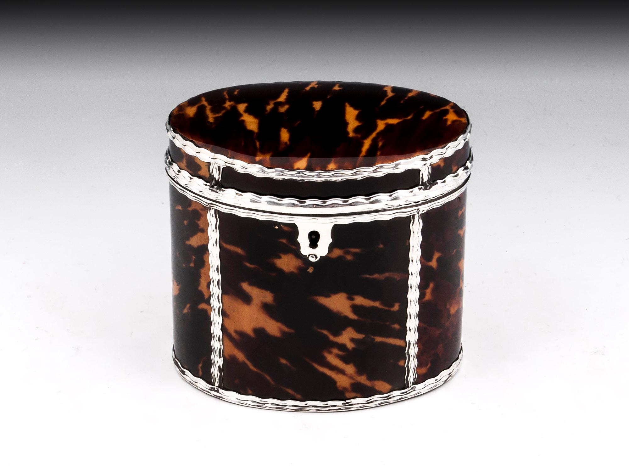 Small oval tortoiseshell Tea Caddy with applied pressed silver with a rippled design. The front has an ornate silver escutcheon. The tortoiseshell & silver tea caddy interior contains most of its original tin lining with a rippled silver surround
