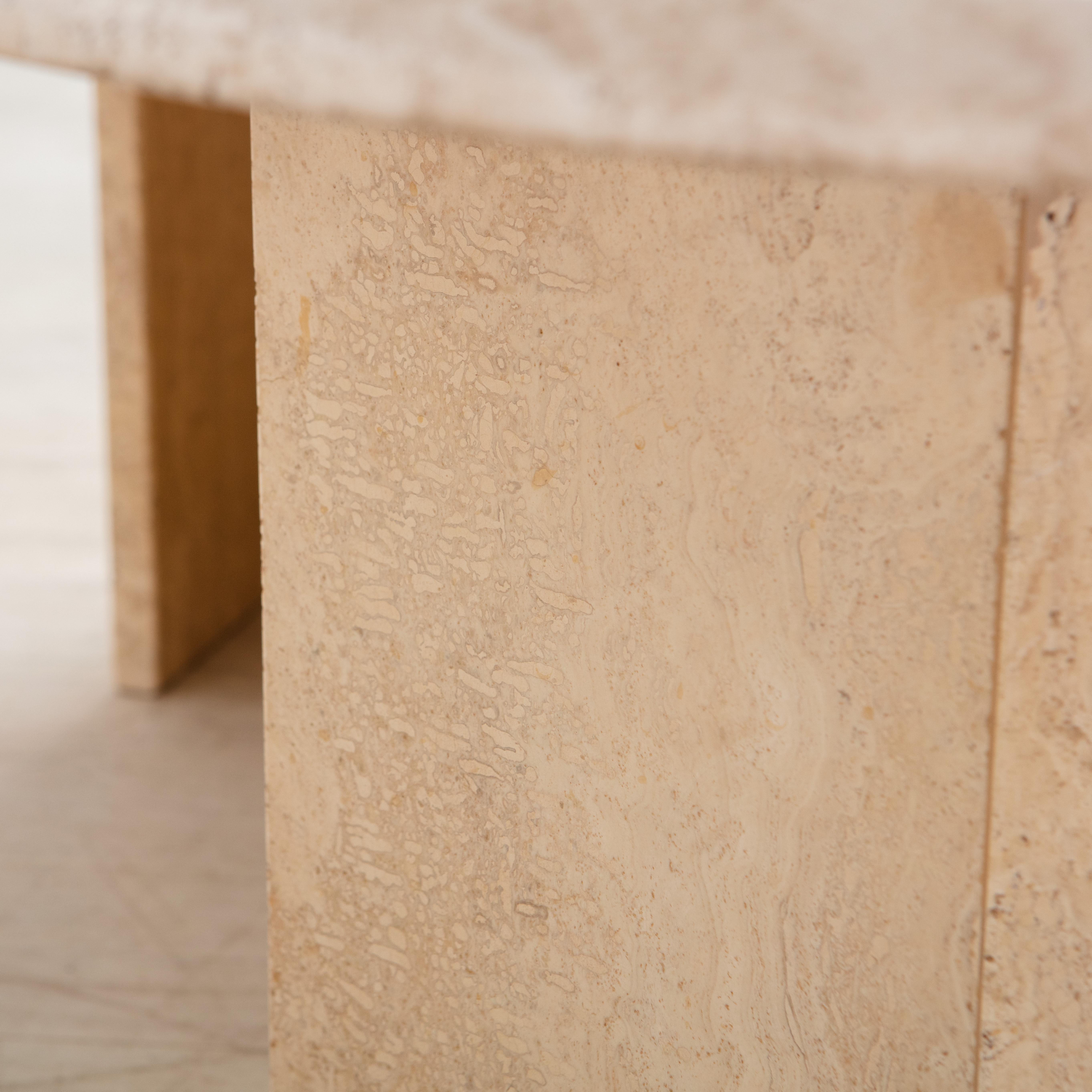 A vintage travertine coffee table featuring an oval top with a lovely beveled edge, which rests on two angular travertine bases. Sourced in France.