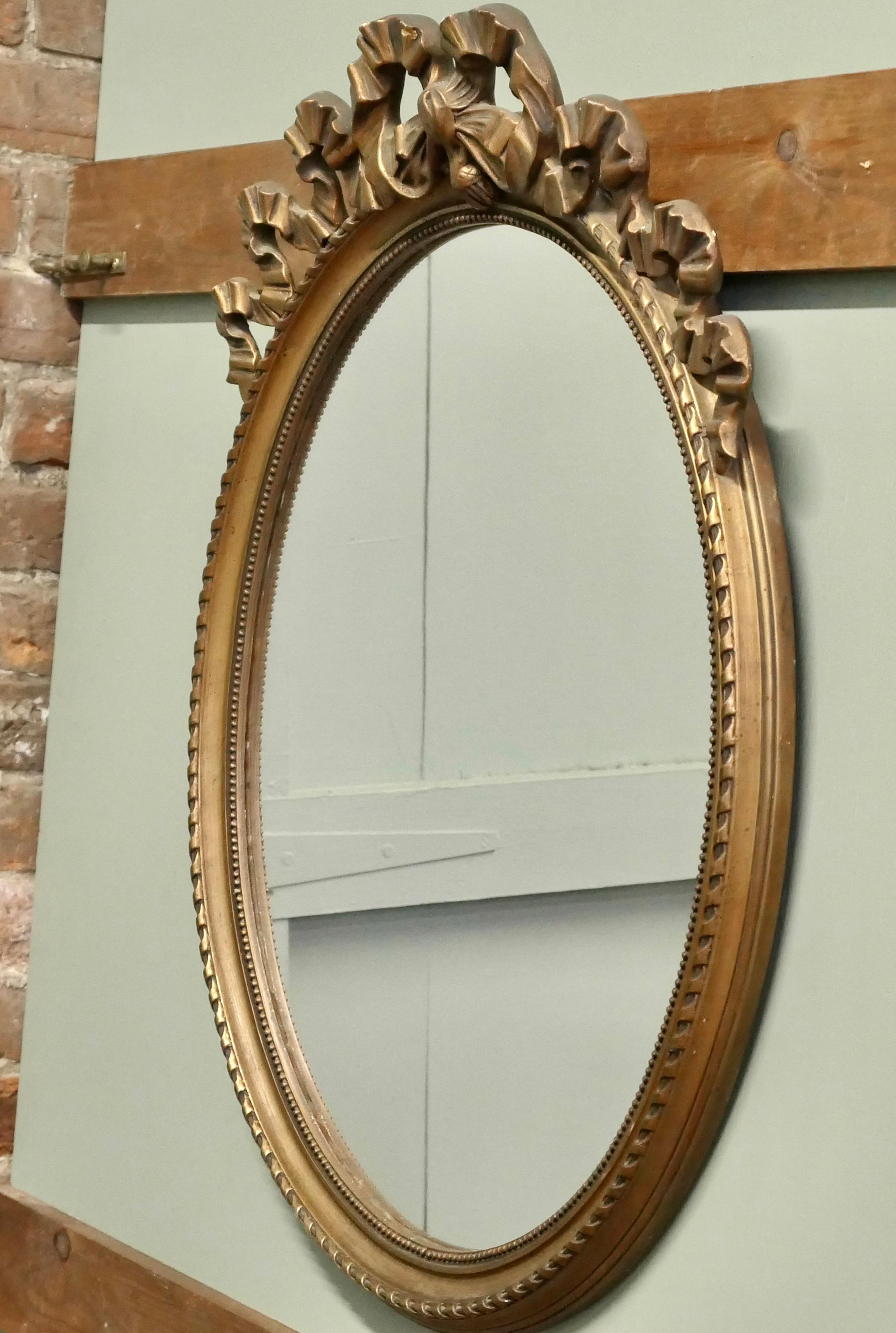 Legno dorato Specchio ovale da parete dorato e decorato con nastri  Un pezzo incantevole in vendita