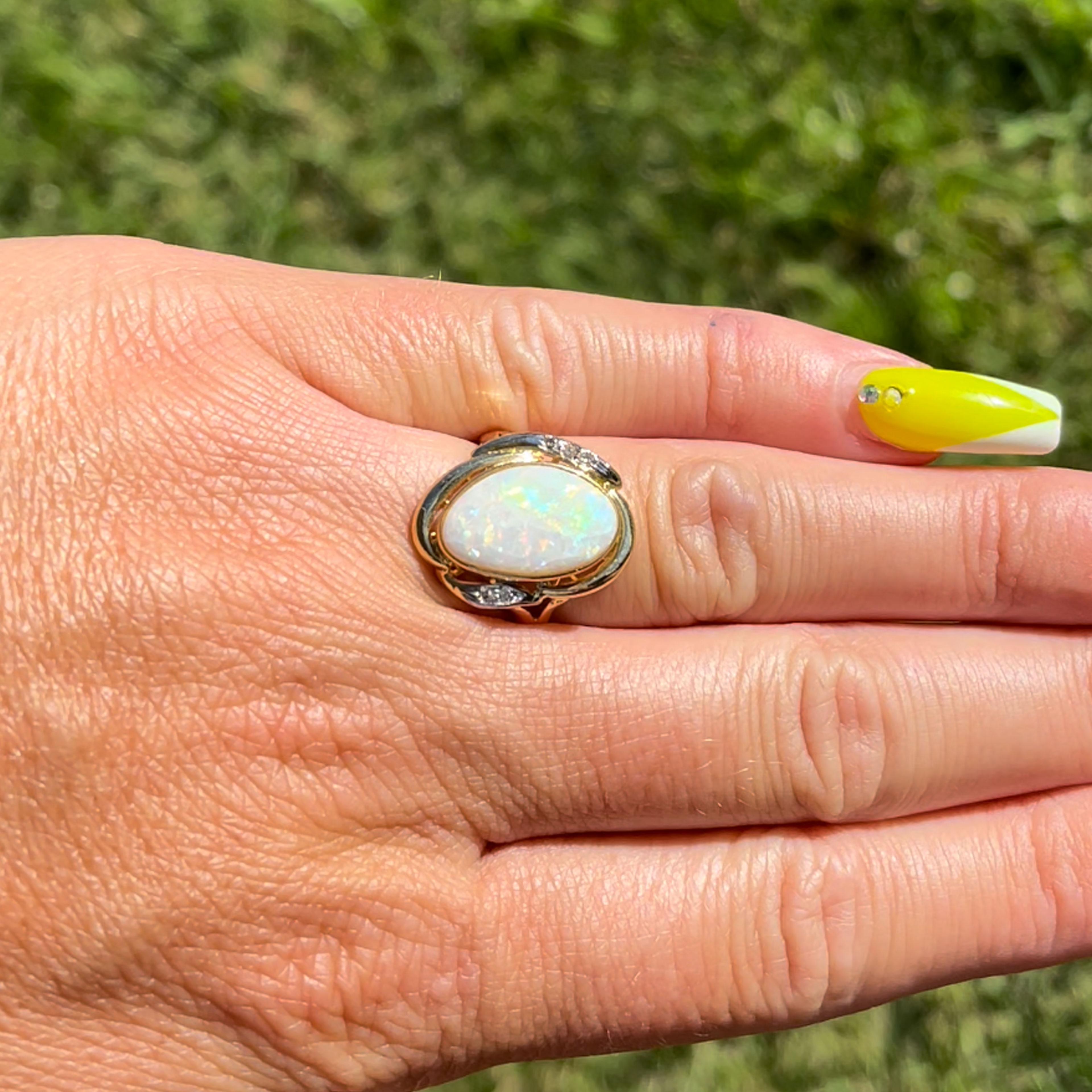 White Opal and Diamond split shank ring  in 14k Yellow Gold. The oval free form opal is bezel set and measures approximately 15.3mm x 9.5mm x 2.2mm. The white Ethiopian opal has a beautiful color play with green, blue and orange color flashes and