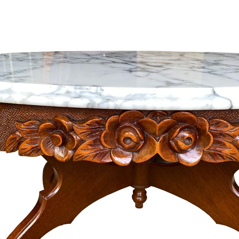 A fine Victorian-style oval coffee or drinks table. The top is created from white marble with incredible dark grey veining and a beveled edge. The top is removable from the base. The base has four wood legs, with an intricately carved floral motif