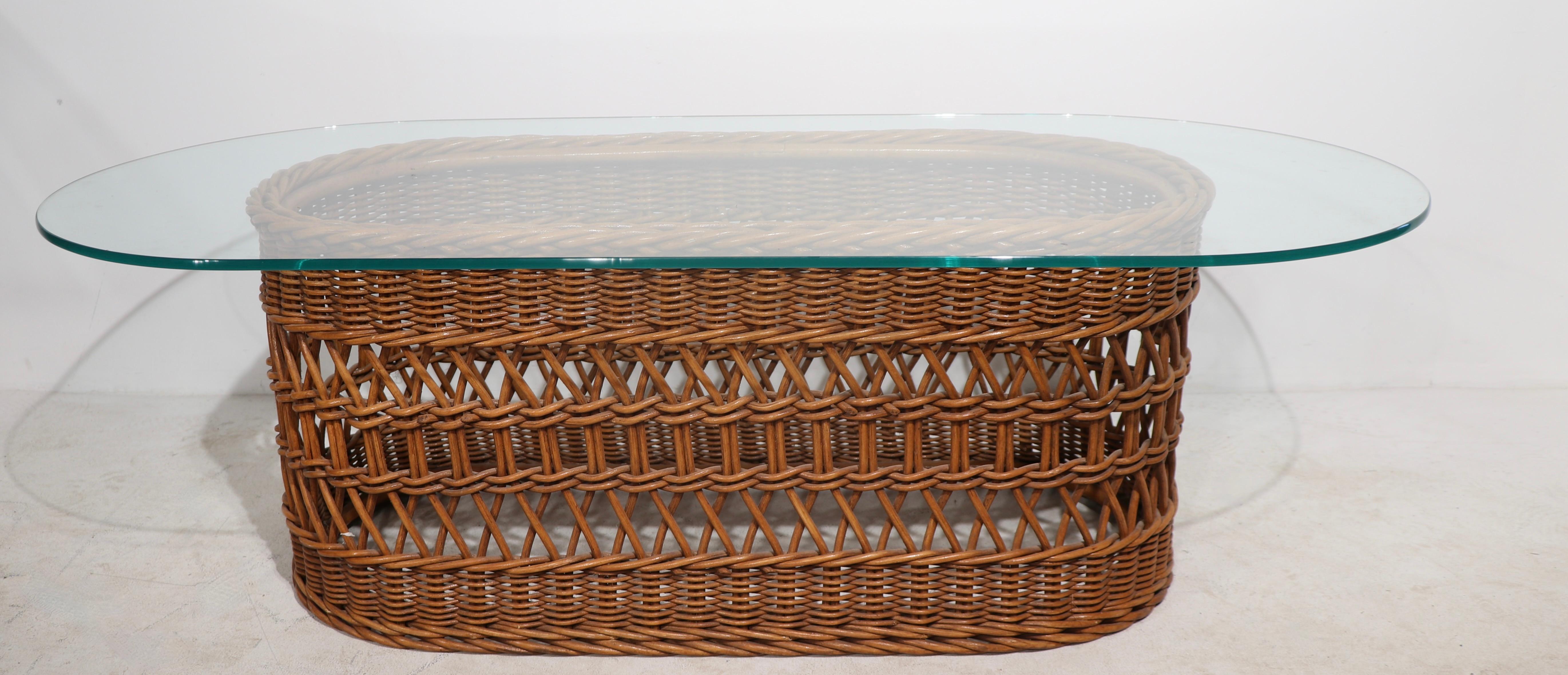 Chic woven wicker and plate glass coffee table in very fine, original condition, clean and ready to use. The oval glass top ( 54 W x 24 D in. ) rests on an oval wicker base ( 37.5 W x 17 D in. ).
