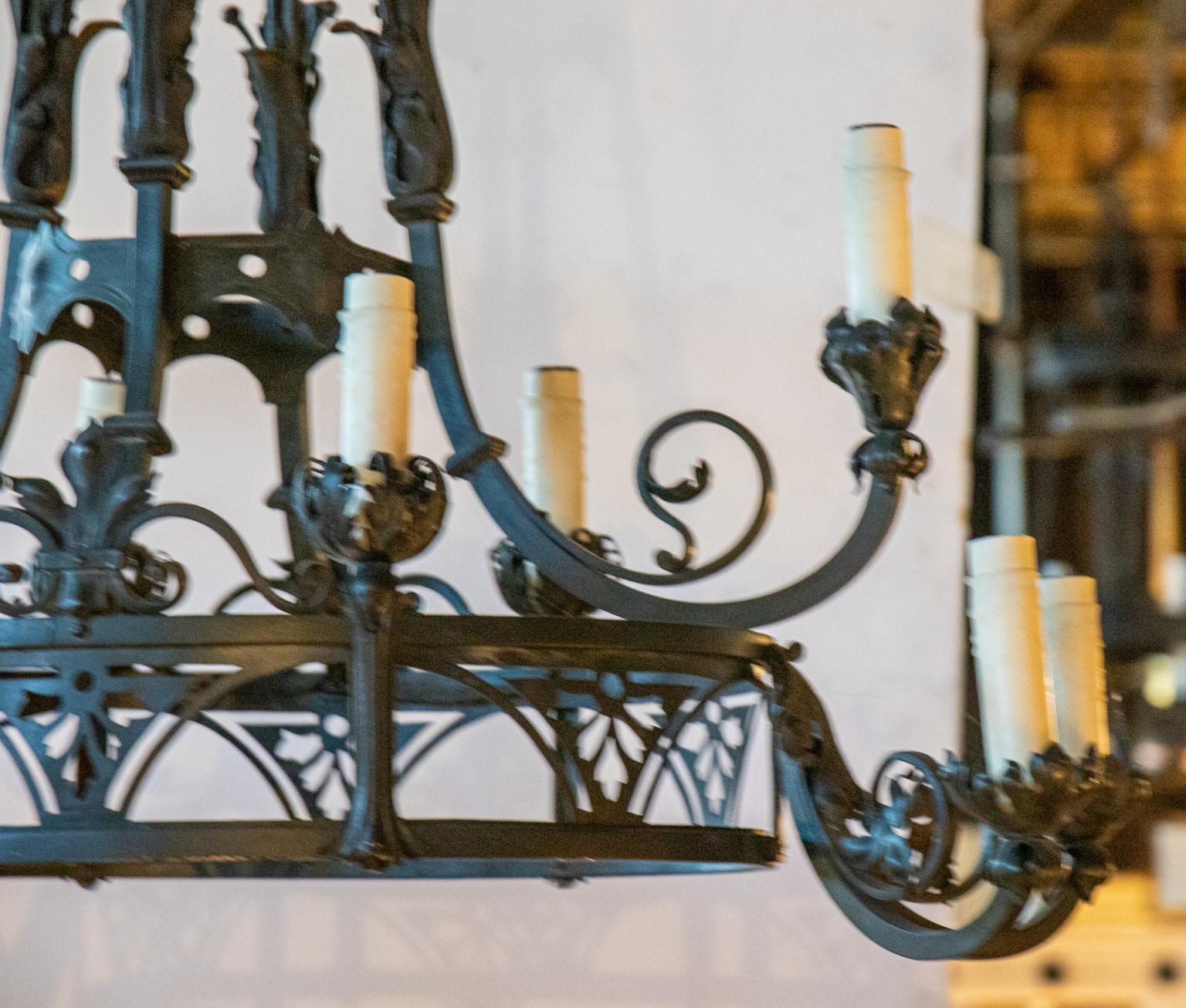 Oval shaped wrought iron painted two tier chandelier in the Gothic Revival style with scrolled acanthus leaf bobeches and pierced floral tracery on the oval frame. Please note of wear consistent with age including patina to the metal. Shades not