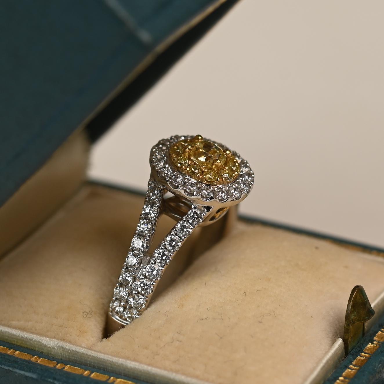 This ring features an approximately 0.20 carat oval-cut yellow diamond of VS1 clarity as its centerpiece. Surrounding the vibrant stone is a striking double halo of yellow and white diamonds, designed to maximize brilliance and color contrast.

The