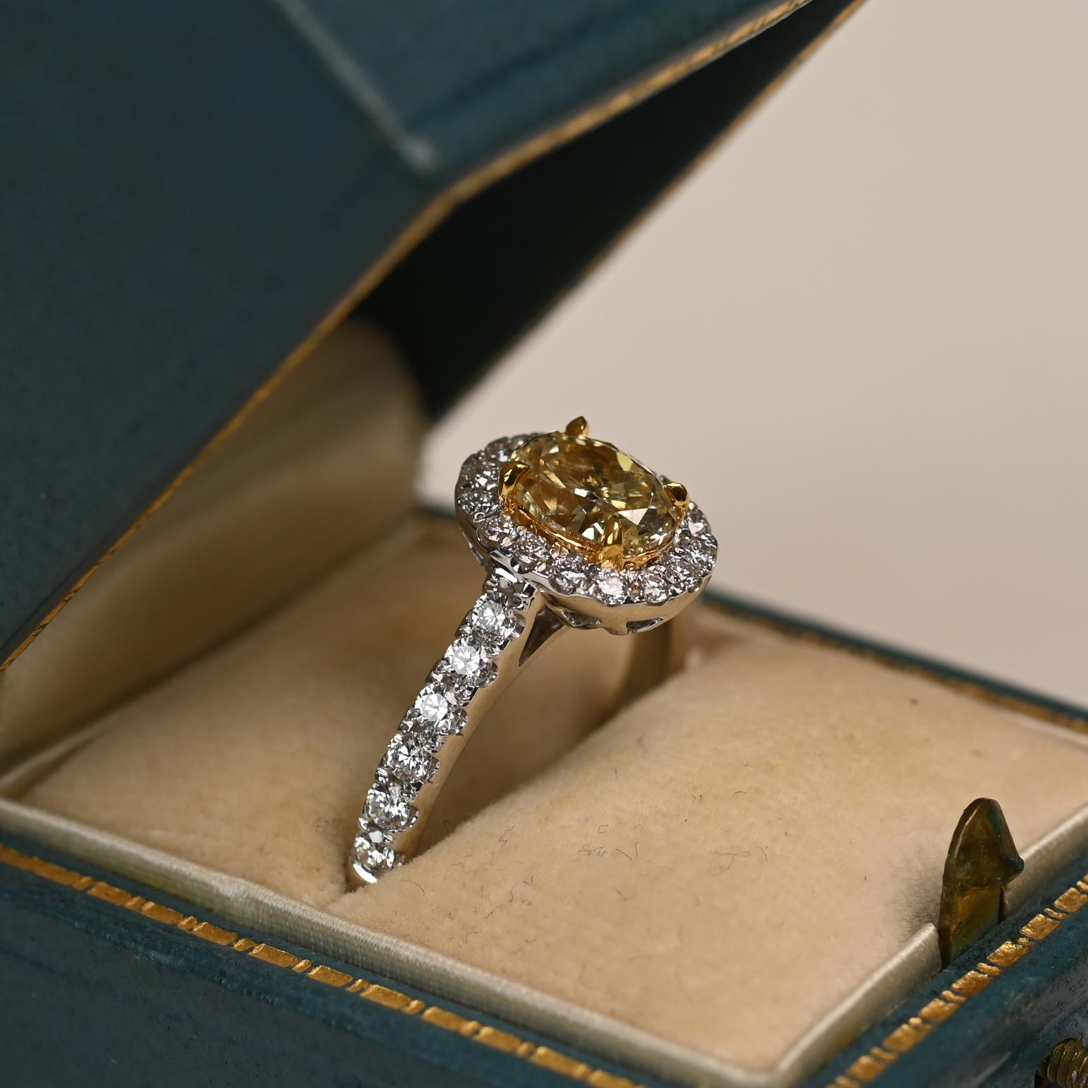 This elegant ring features an approximately 1.10 carat oval cut yellow diamond of VS1 clarity, securely set in a yellow gold prong setting. Surrounding the vibrant center stone is a halo of sparkling white diamonds, enhancing its brilliance and