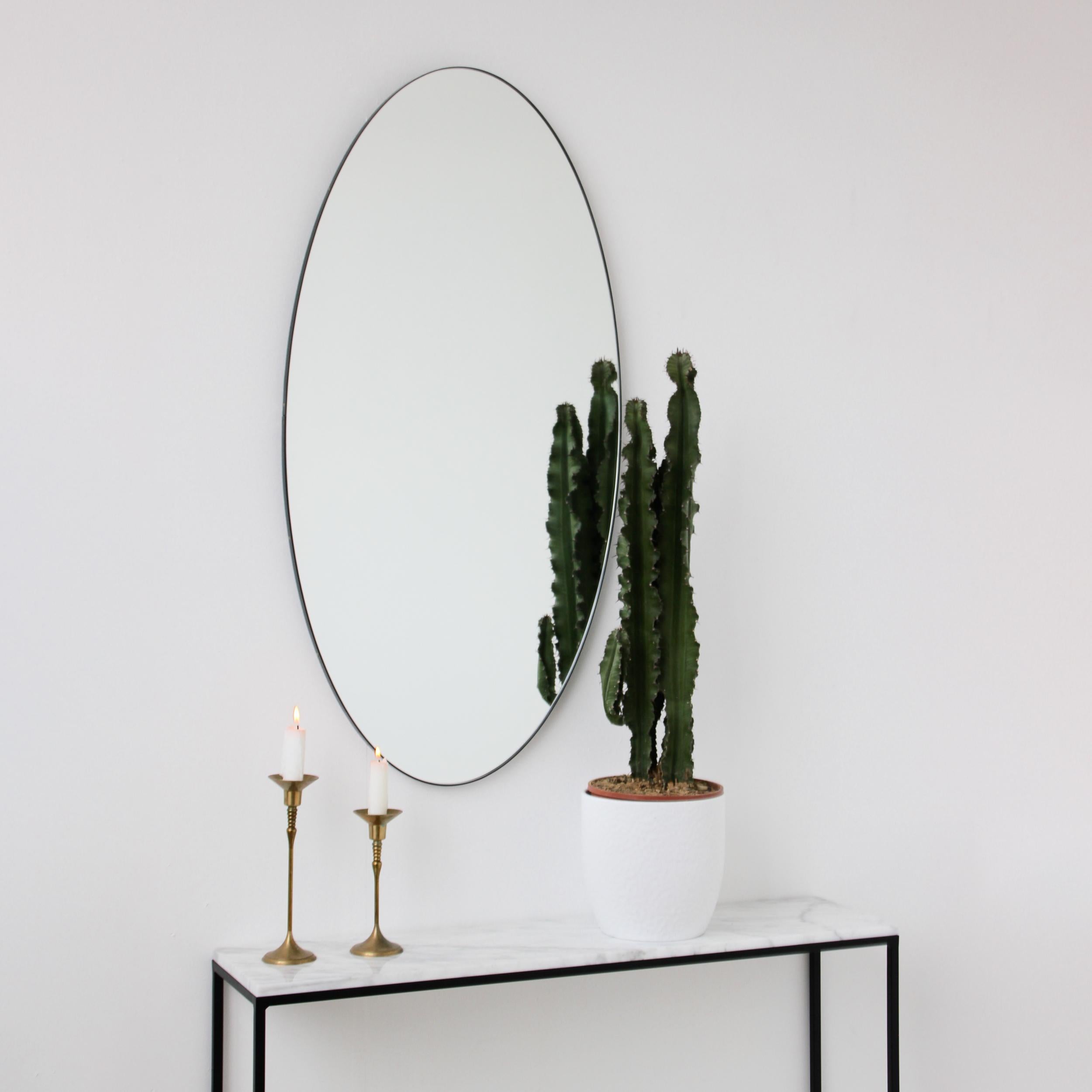 Grand miroir ovale minimaliste avec un cadre contemporain en aluminium peint par poudrage en noir. Conçu et fabriqué à la main à Londres, au Royaume-Uni.

Nos miroirs sont conçus avec un système intégré de tasseaux français (lattes fendues) qui
