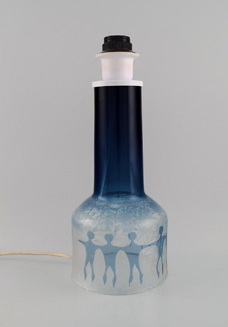 Ove Sandberg for Kosta Boda. 
Two table lamps in blue and clear art glass decorated with people. 1970s.
Measures: 29 x 15 cm (ex socket).
In excellent condition.
Signed.