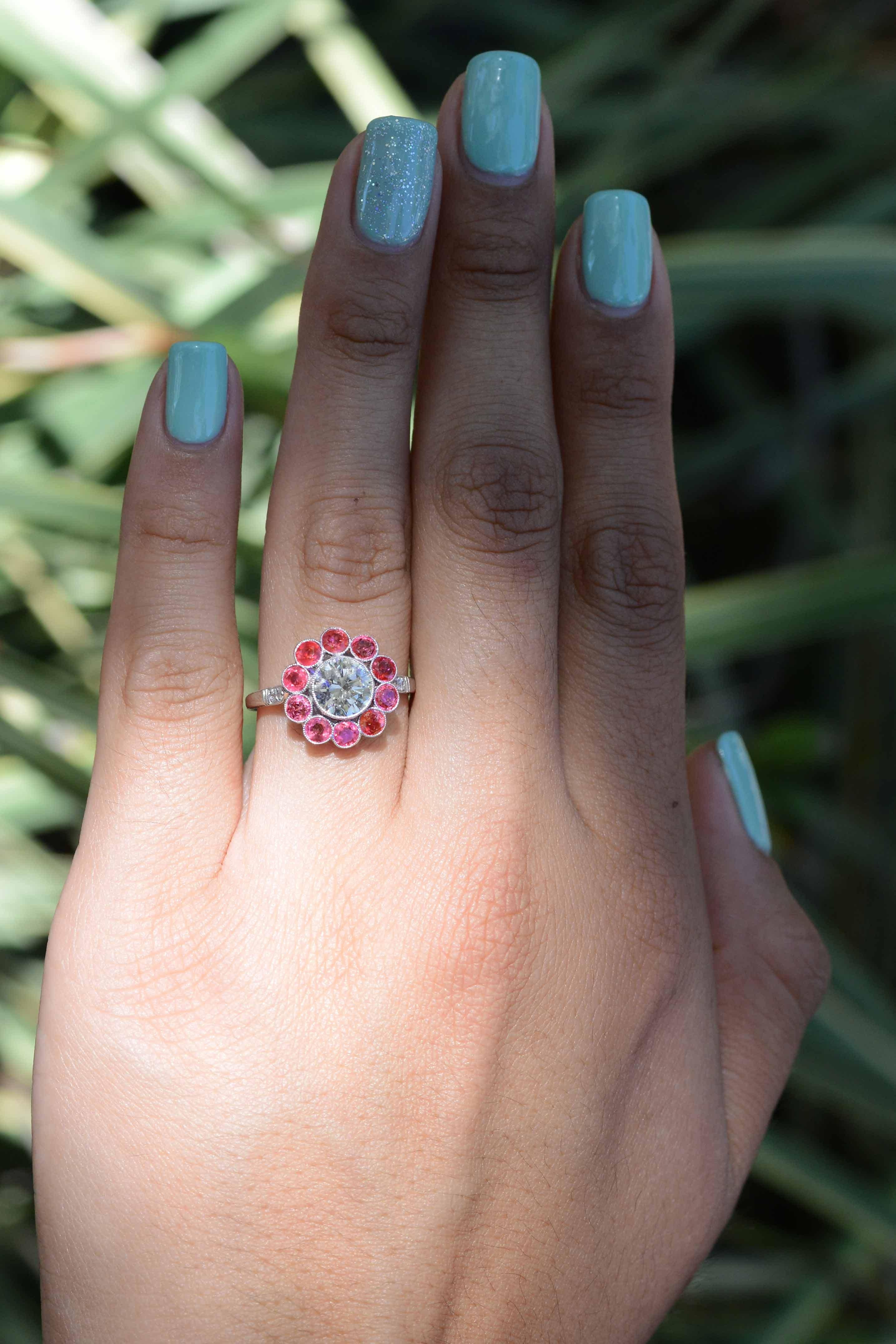 This diamond and ruby halo flower engagement ring throws a subtle twist on a classic design. Centered by a dazzling round brilliant cut diamond of 1.11 carats and adorned with 10 bright ruby 