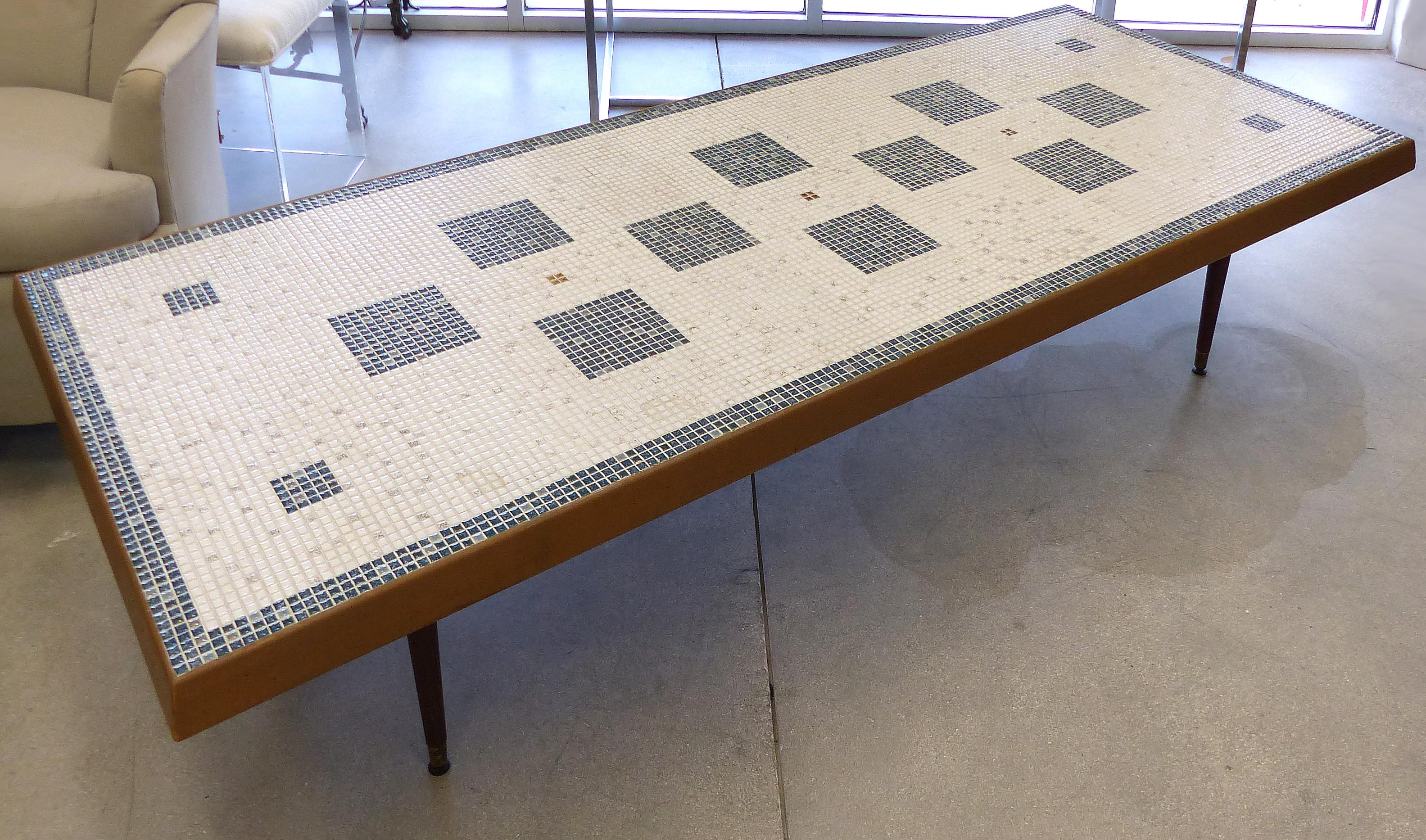 Offered for sale is an over-scale Mid-Century Modern tile top coffee table with a geometric pattern tiles in blue and off-white with gold accents. The table is banded in wood and has four tapering conical feet with brass caps.