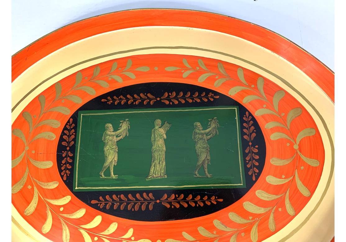 Mesa bandeja pintada de mediados de siglo de 1960, Made in Italy. La bandeja de metal con vibrantes colores rojo y verde con adornos dorados y detalles de diseño y asas recortadas. Bandeja con tres figuras neoclásicas y hojas de laurel. 

Medidas:
