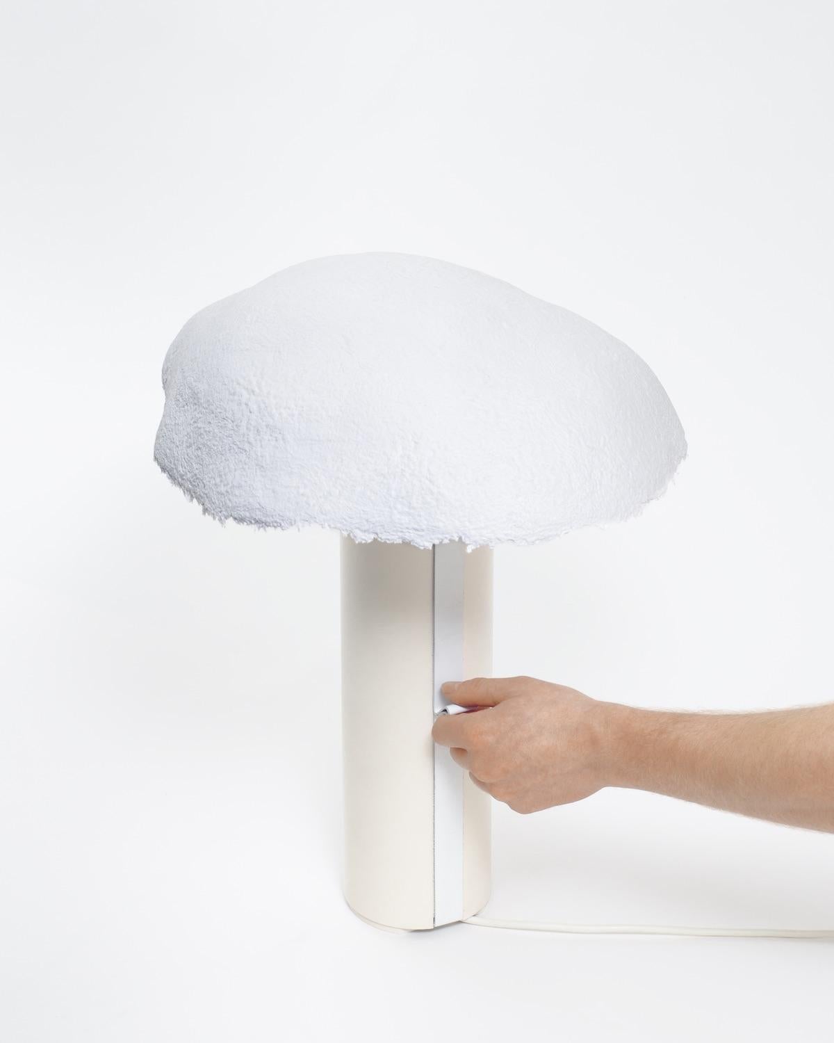 The overcast light consists of an aluminum cylindrical base and a paper shade. The shade is Handmade from blended paper pulp that allows light to shine through mimicking the effect of the sun obscured by cloud cover. Every shade's lower rough hewn