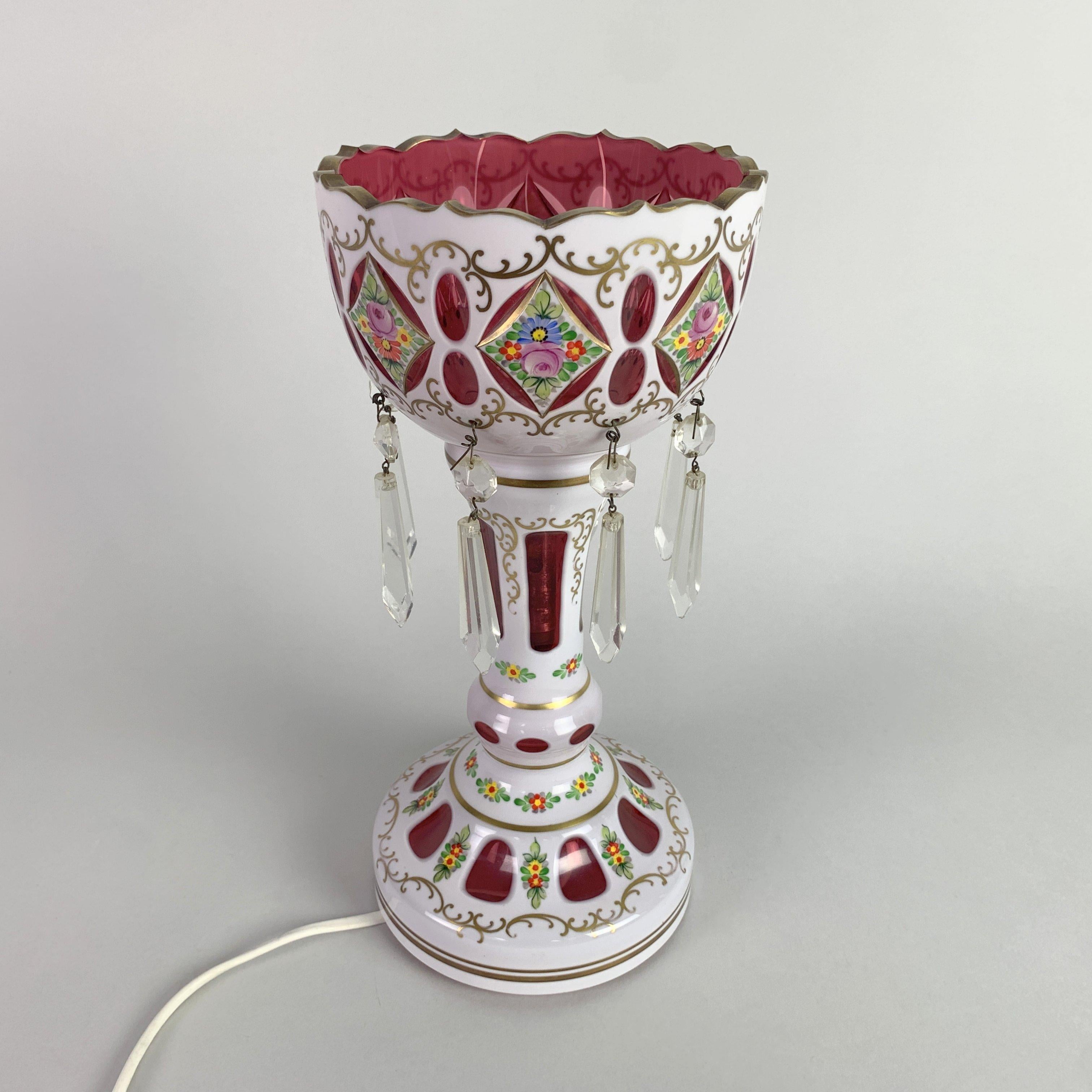 Bohemian glass lustre lamp with hand painted floral decoration with gilt accents. Ruby underlay with white overlay and enameled glass, bearing eight cut glass pendants. One of the pendants is unfortunately chipped (see photo), but overall the lamp