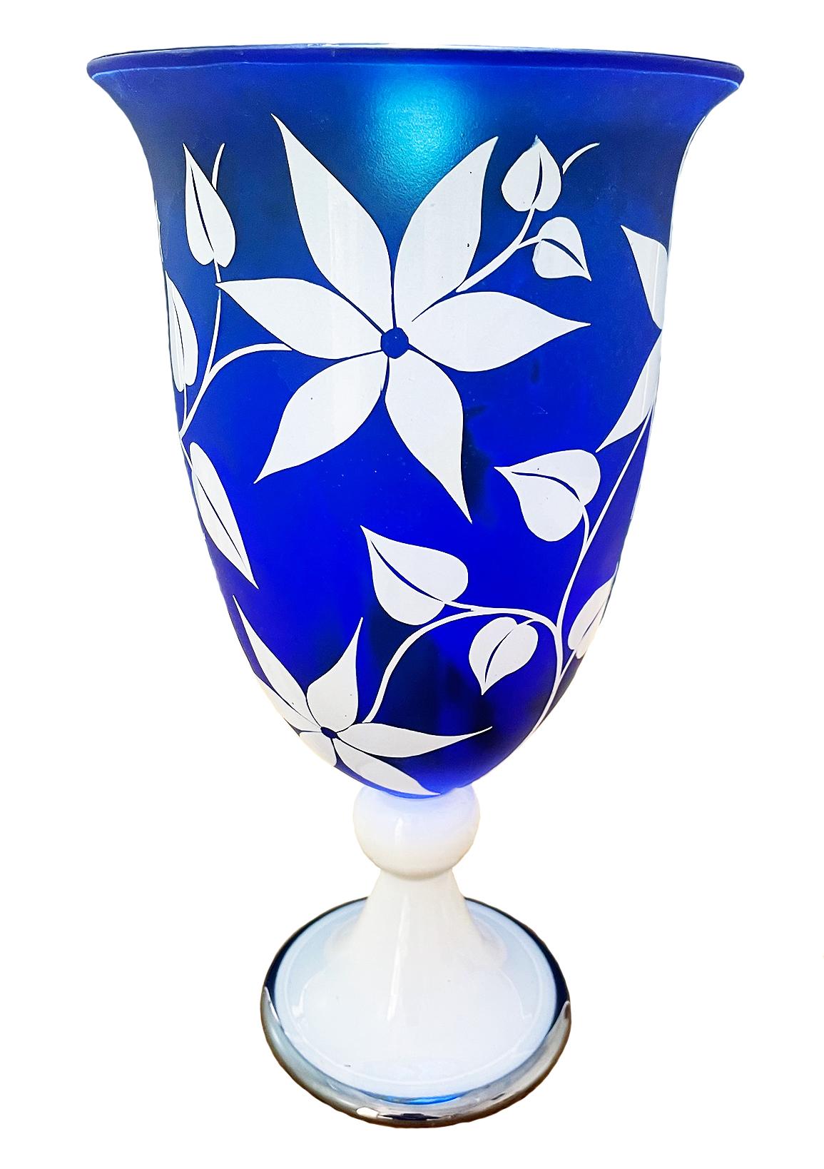 This cameo etched vessel by Gary Genetti is overlay blown glass. It features a cobalt blue background to enhance the graphic white overlay. The original artwork is drawn on the piece, hand cut then pressure etched through layers of color to create