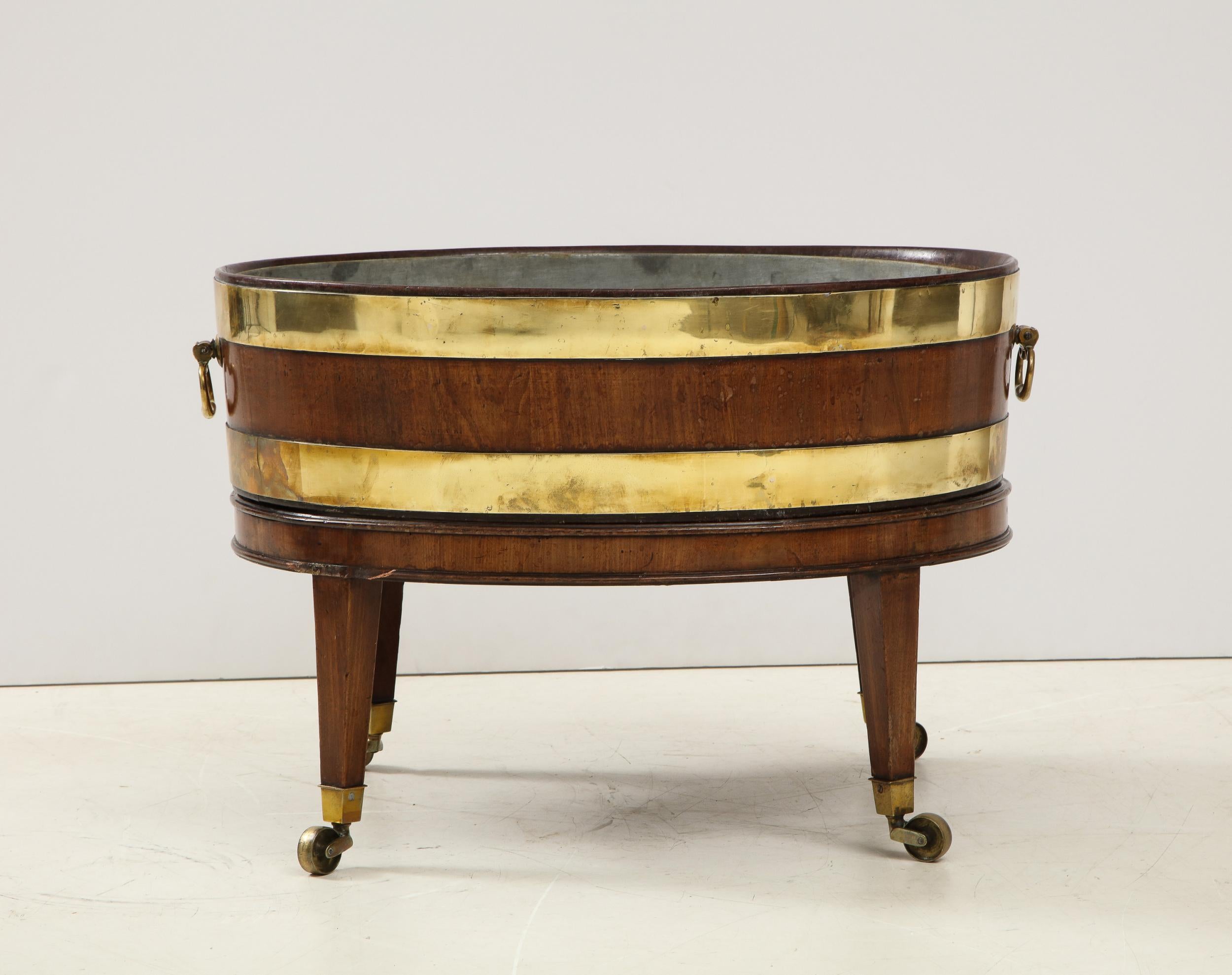 Fine George III oval wine cooler or cellarette of unusually large scale, of staved construction and with two brass bands and original carying handles, the stand with double bands of molding on splayed tapered legs ending in original box casters, the