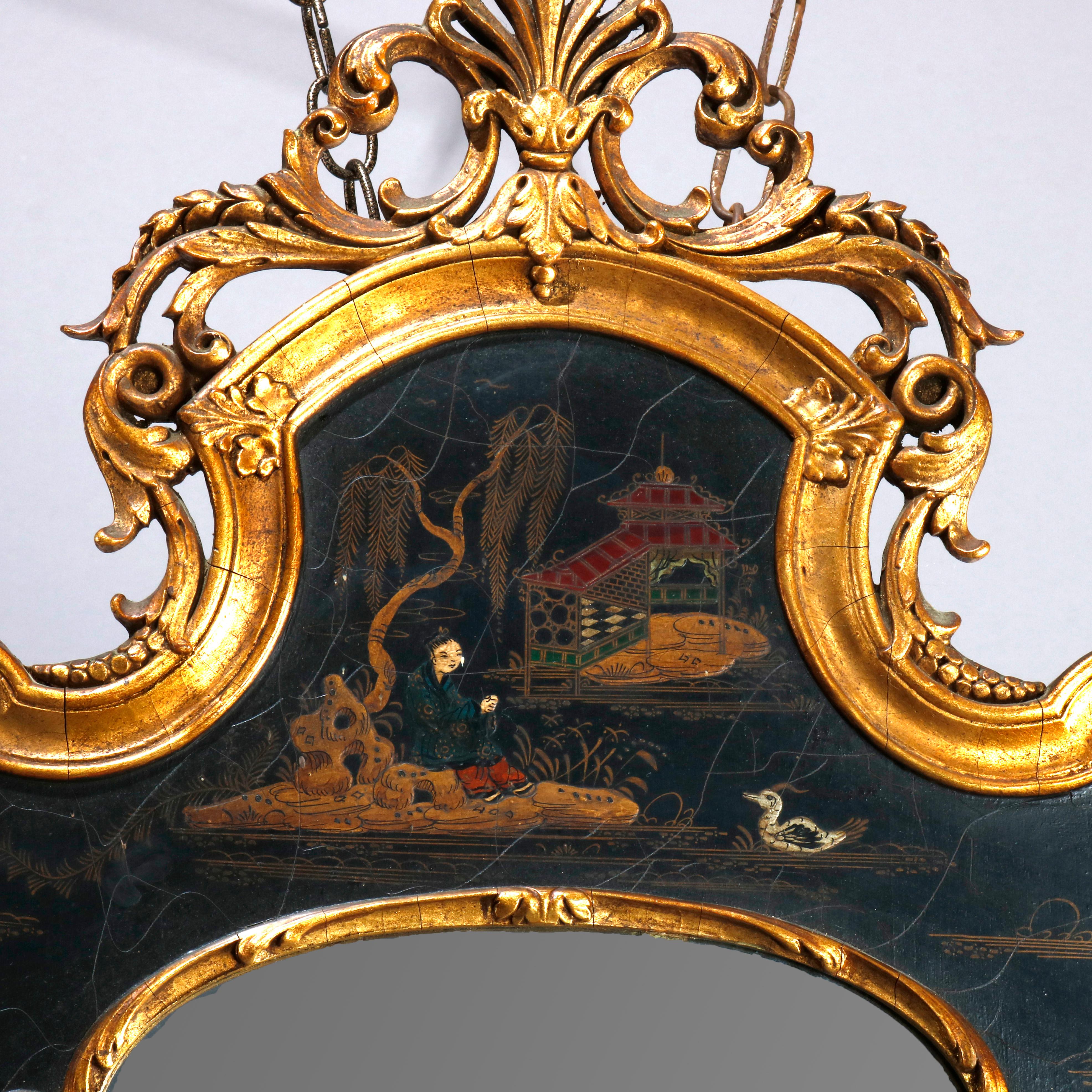 An antique and oversized English Georgian style wall mirror offers giltwood and ebonized frame with pierced crest having central palmette flanked by foliate elements and hand painted chinoiserie decorated landscape scene with pagoda, lake and duck