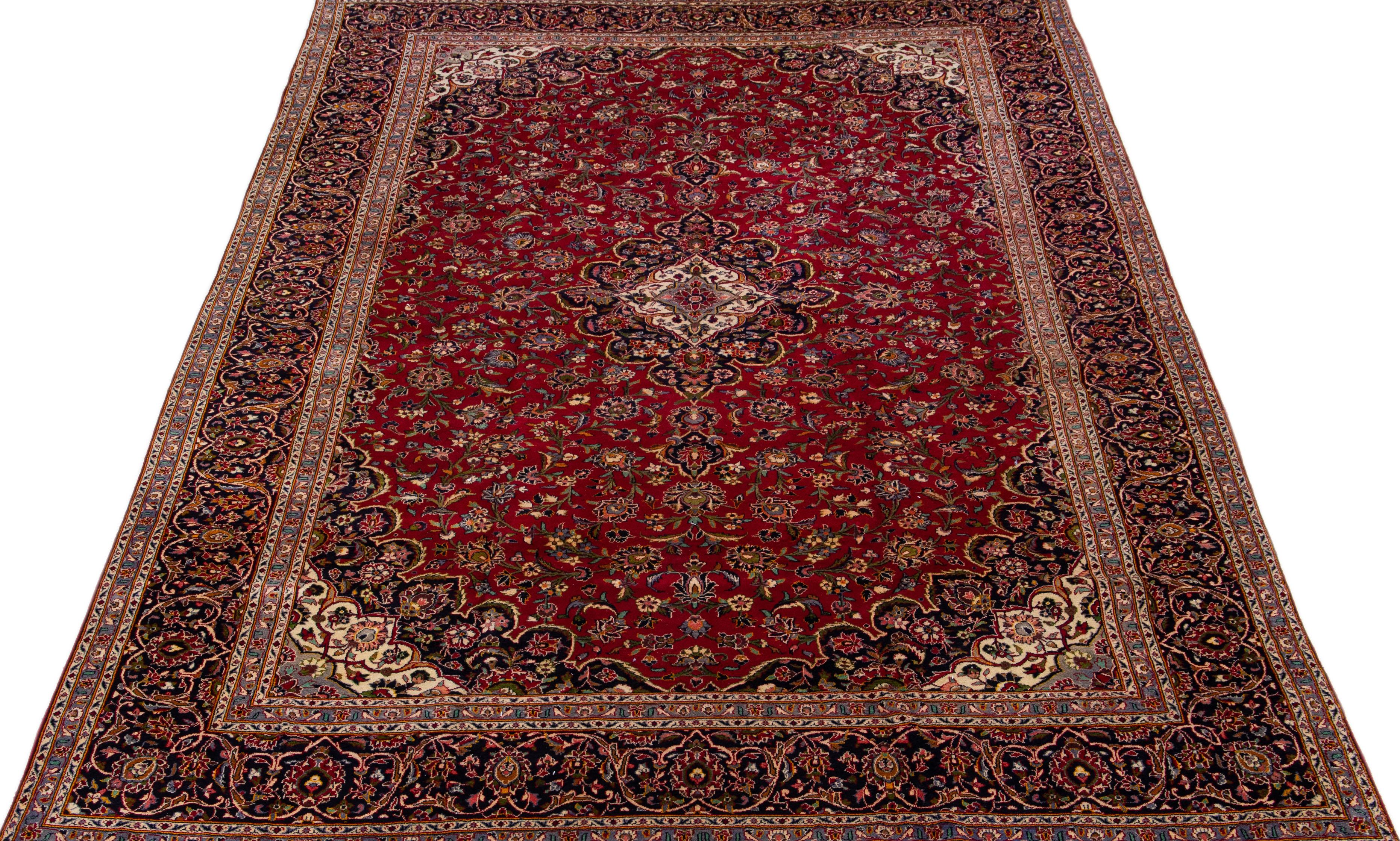 Beautiful antique Kashan hand-knotted wool rug with a red color field. This Persian rug has a navy blue frame and multicolor accents in a gorgeous all-over medallion floral design. 

This rug measures 11' x 16'8