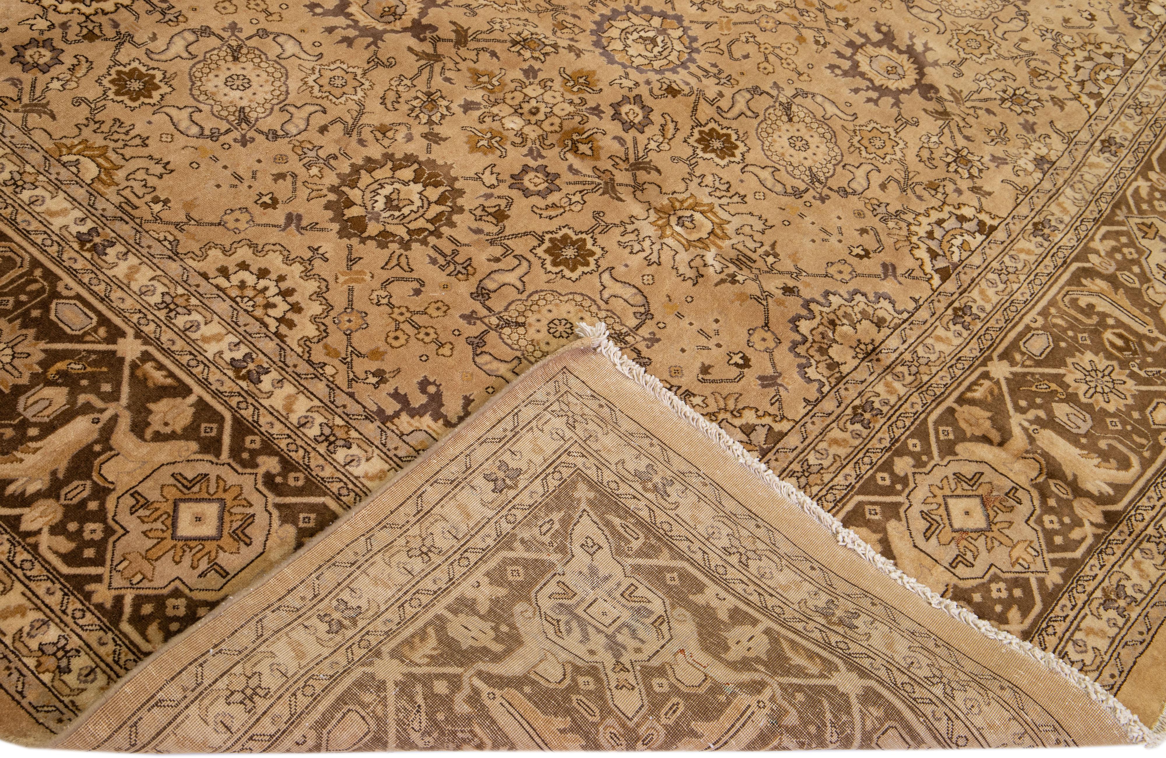 Magnifique tapis antique Tabriz en laine nouée à la main avec un champ brun clair. Cette pièce persane présente des accents verts, bruns et beiges dans un magnifique motif floral. 

Ce tapis mesure : 11' x 18'9