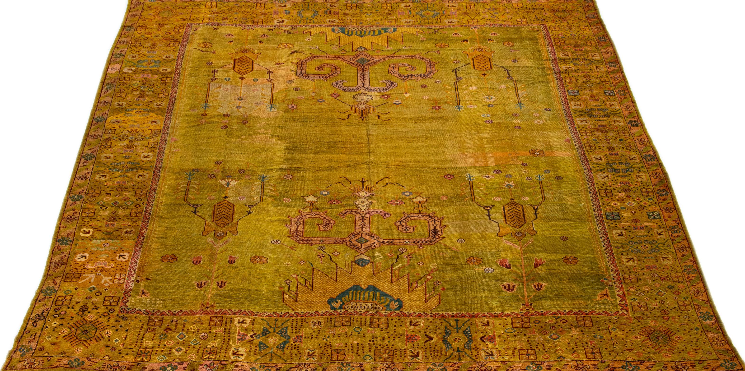 Dieser exquisite handgeknüpfte quadratische Wollteppich aus der türkischen Oushak Collection des 19. Jahrhunderts zeichnet sich durch ein atemberaubendes olivgelbes Farbfeld aus, das durch elegante blaue und rostfarbene Akzente ergänzt wird, die in