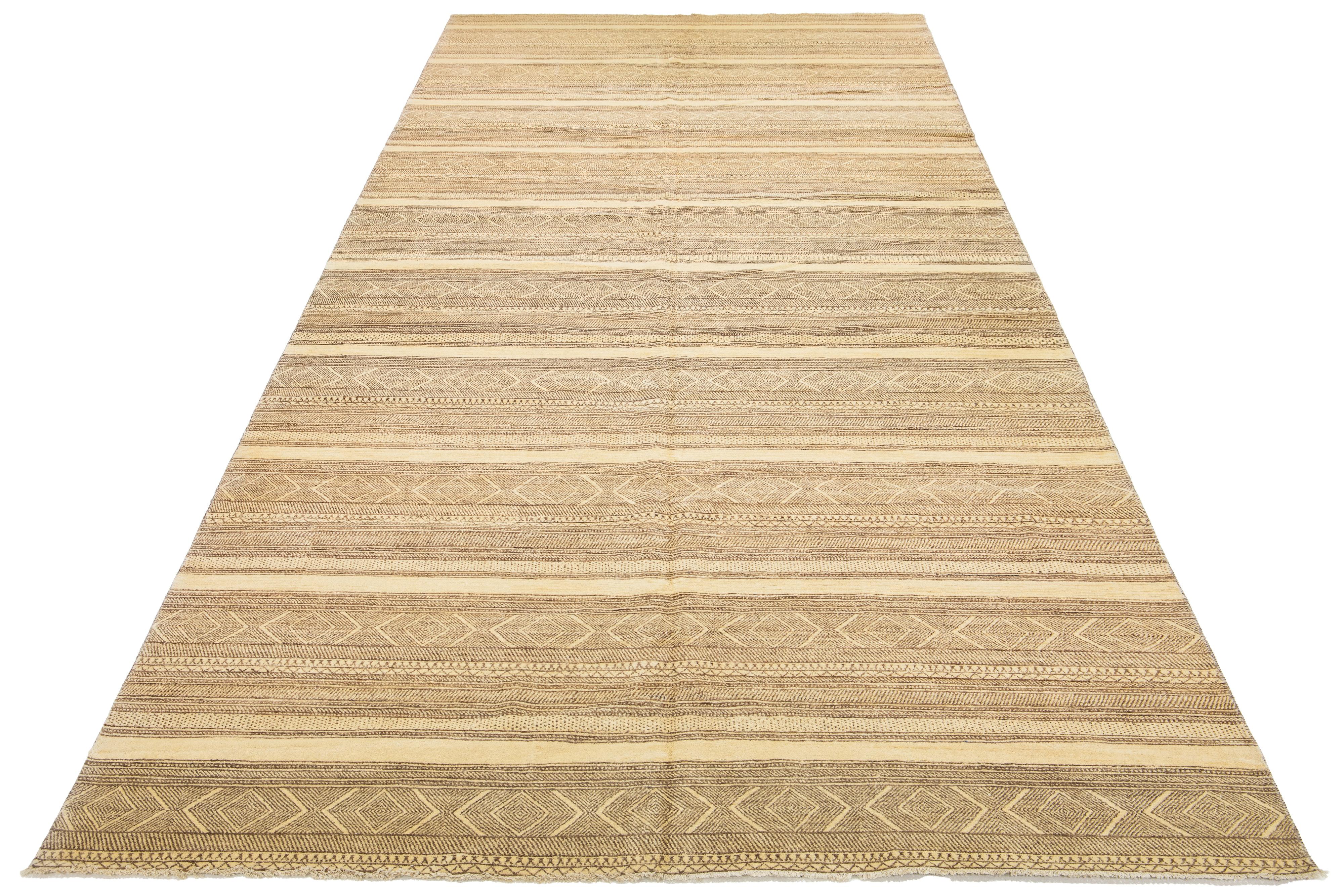 Questo tappeto in lana lavorato a mano, in stile Gabbeh, presenta motivi geometrici con accenti marroni su uno sfondo beige.

Questo tappeto misura 9'2