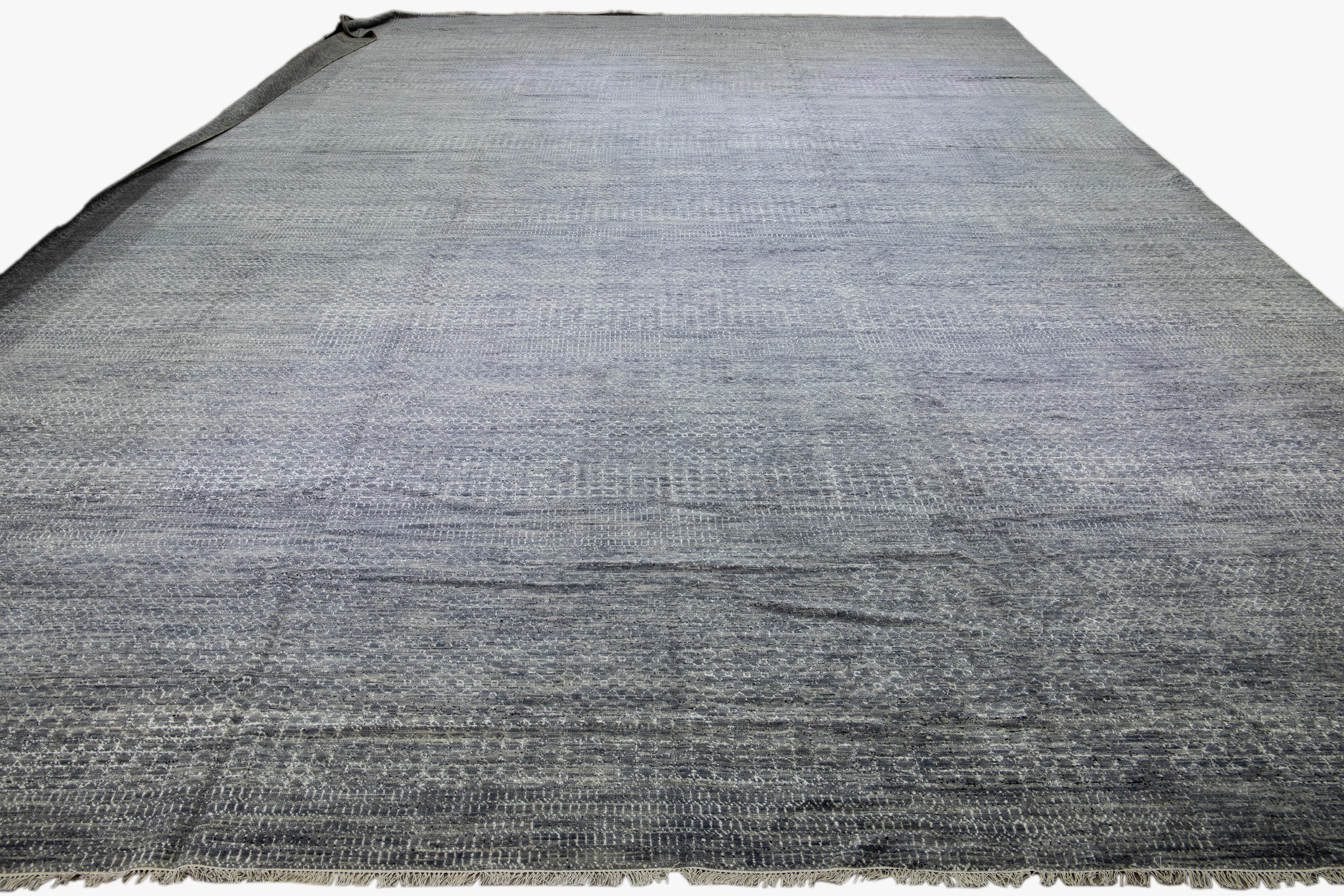 This elegant Shiva collection oversize hand-knotted wool rug features a stunning contemporary design, showcasing a meticulously crafted gray field with intricate ivory and black geometric patterns.

This rug measures 20'1