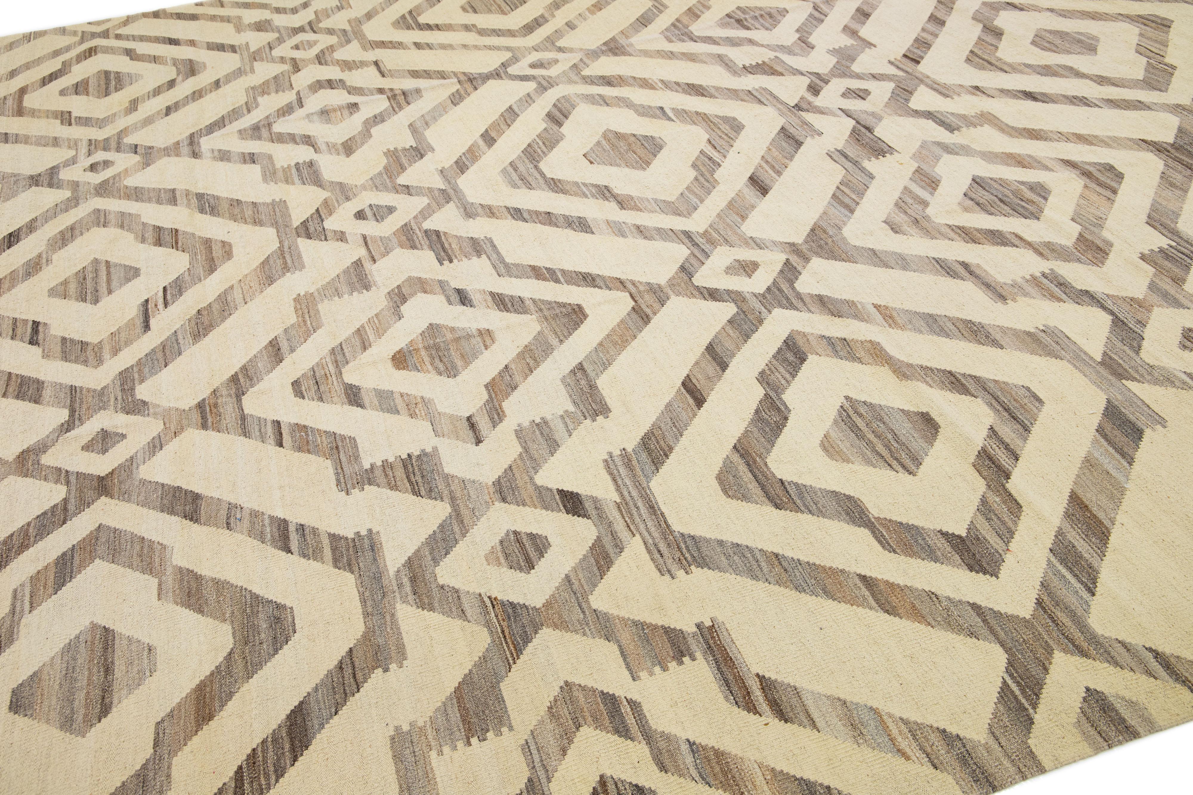 Dieser exquisite Kilim-Teppich zeigt ein modernes geometrisches Muster auf einem neutralen beigen Hintergrund und wurde fachmännisch aus handgeknüpfter Wolle hergestellt. Dieses Stück ist eine atemberaubende Ergänzung zu jedem modernen Dekor,
