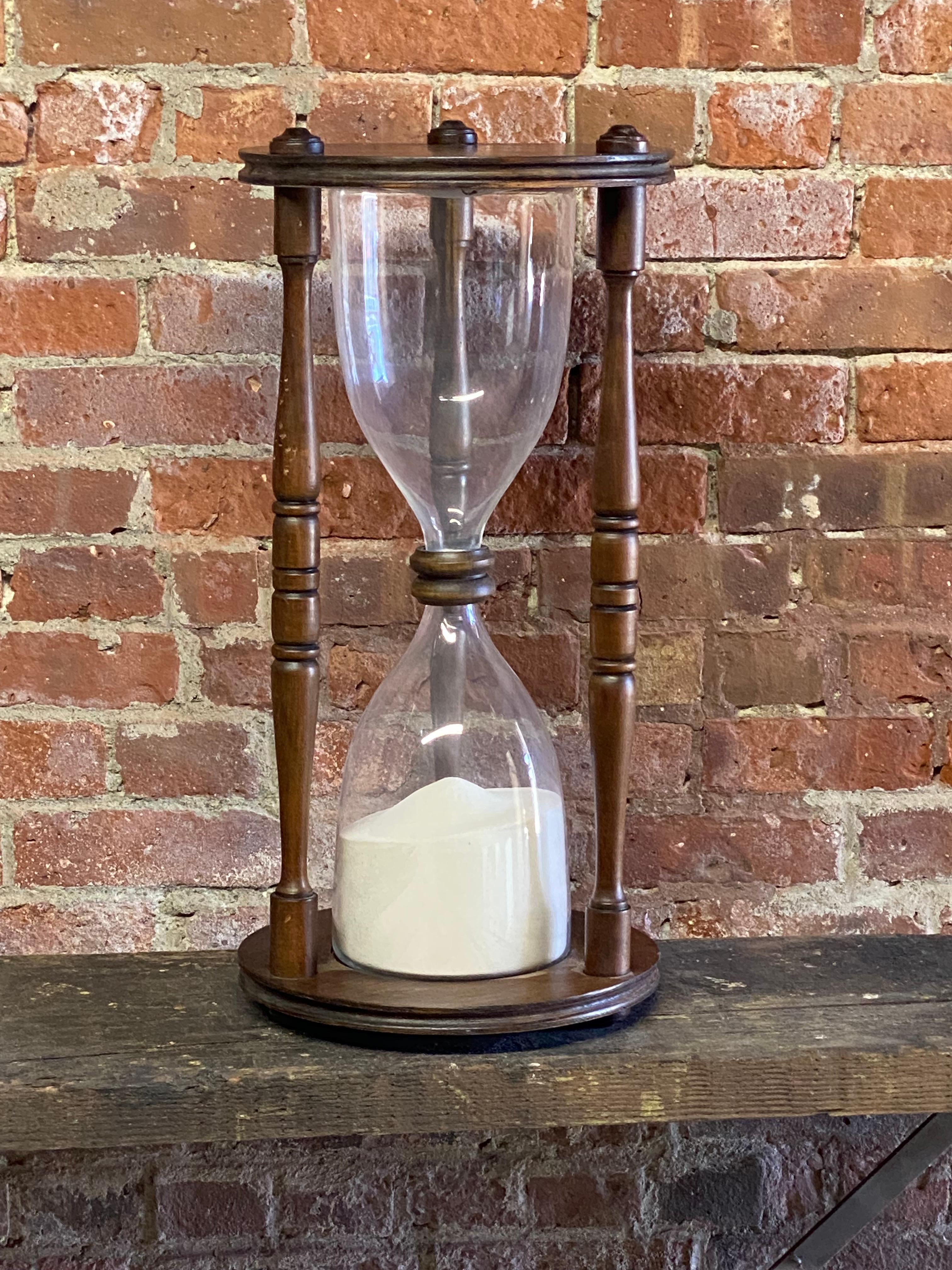 Late 20th Century oversized hourglass. Large and impressive time piece with a wood structure with a dark walnut finish and a two piece blown glass housing for the sand. The tops are sealed in rubber and have a decorative wood collar.

Good overall