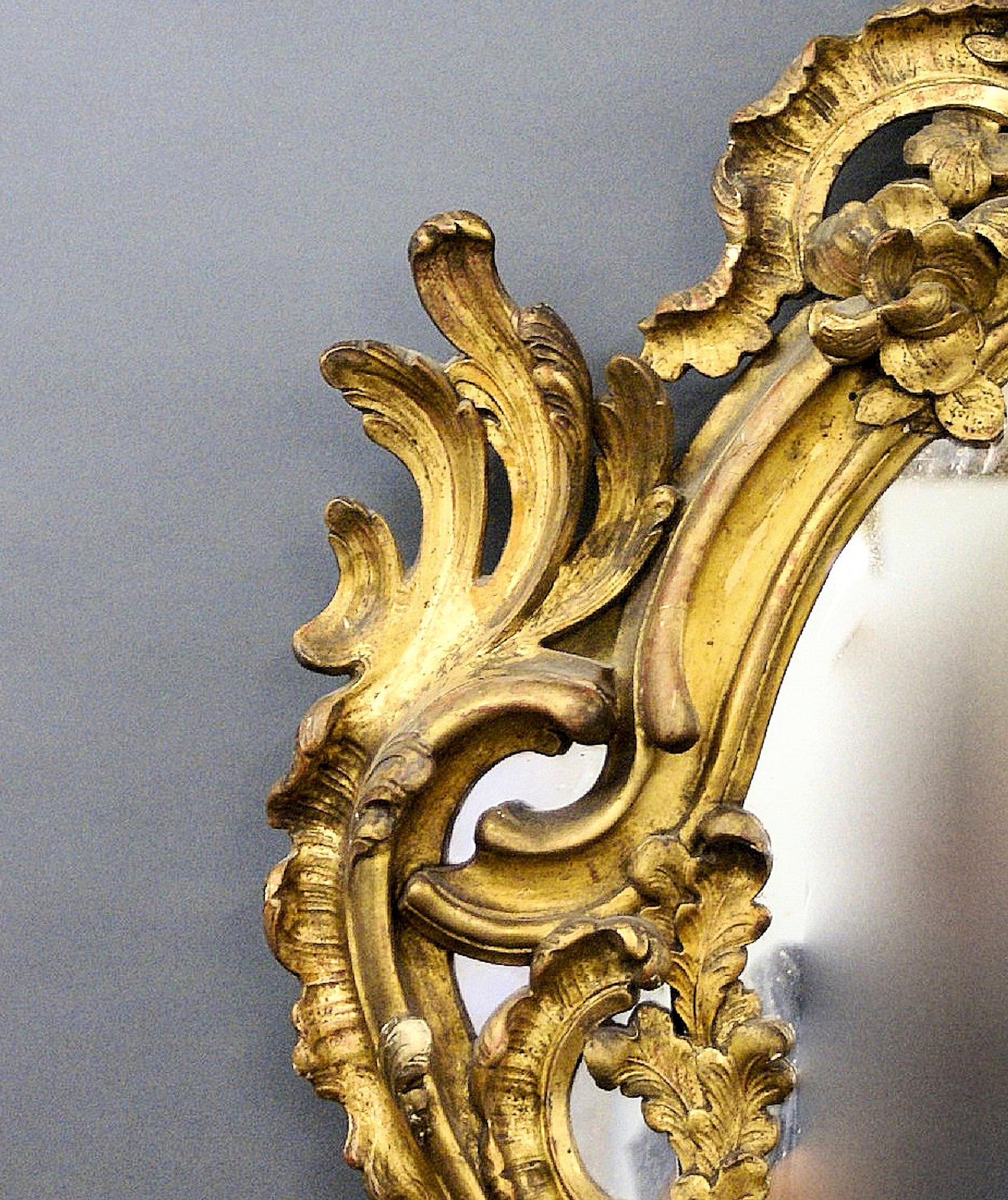 Ce beau et très grand miroir mural français du 19ème siècle en bois sculpté et doré est de style Rococo et conserve sa dorure d'origine, sa plaque de miroir et son support, tous en très bon état. Les marques et les imperfections correspondent à