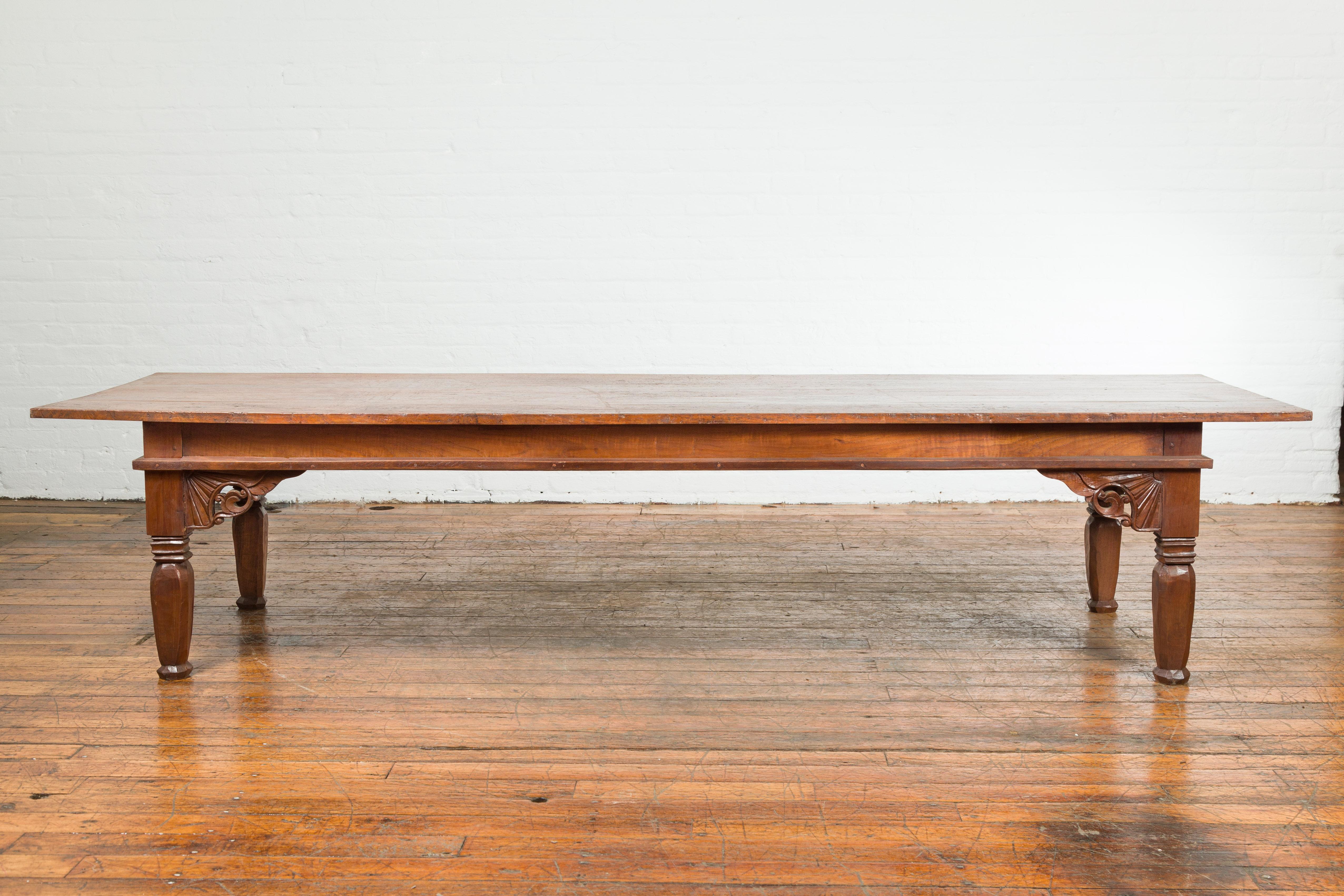 An antique 19th century Indonesian oversized coffee table from Madura, with carved spandrels. Created in Madura off of the northeastern coast of Java during the 19th century, this wooden coffee table features a rectangular planked top overhanging a
