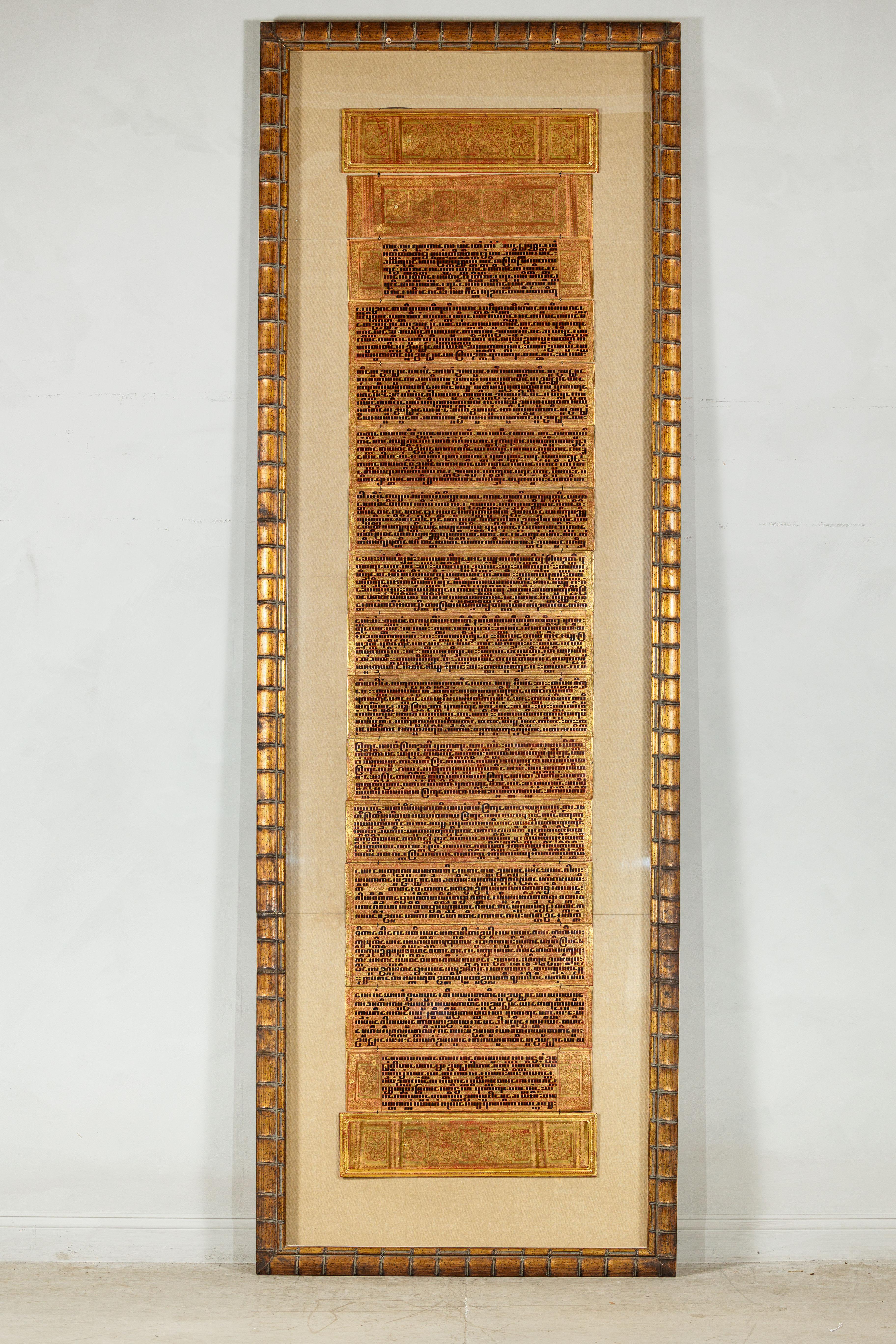 Questa monumentale presentazione incorniciata presenta un antico manoscritto di preghiera birmano, riccamente ornato con decorazioni e scritte dorate, accuratamente montato per essere esposto. Il manoscritto è composto da più foglie unite, ciascuna