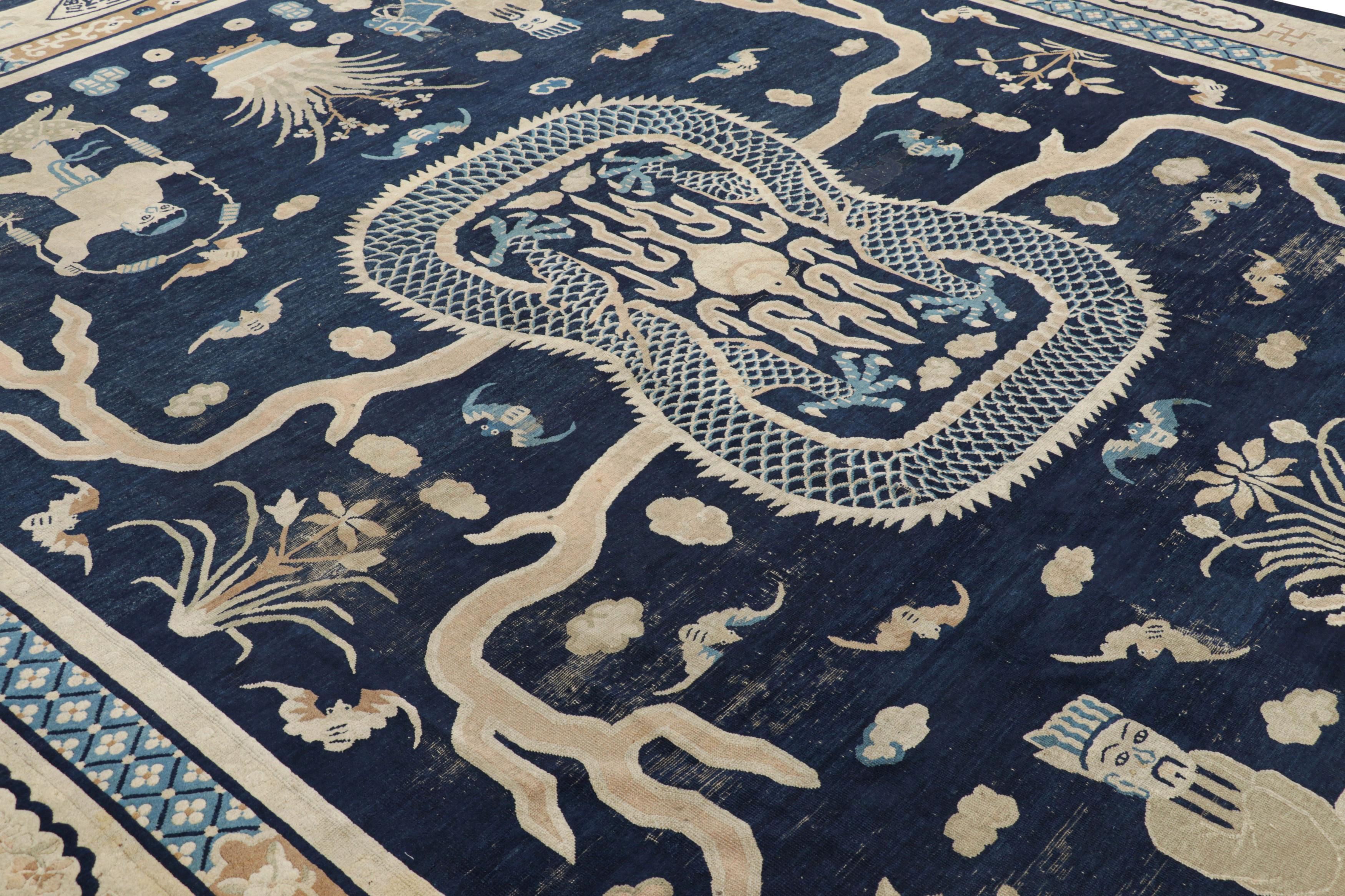 Made with hand-knotted wool and originating from China, this 11x13 oversized antique Peking rug features an intricate symbolic pictorial design with Buddhist and Taoist motifs on a midnight-blue field framed by a formal ivory border—an exciting new