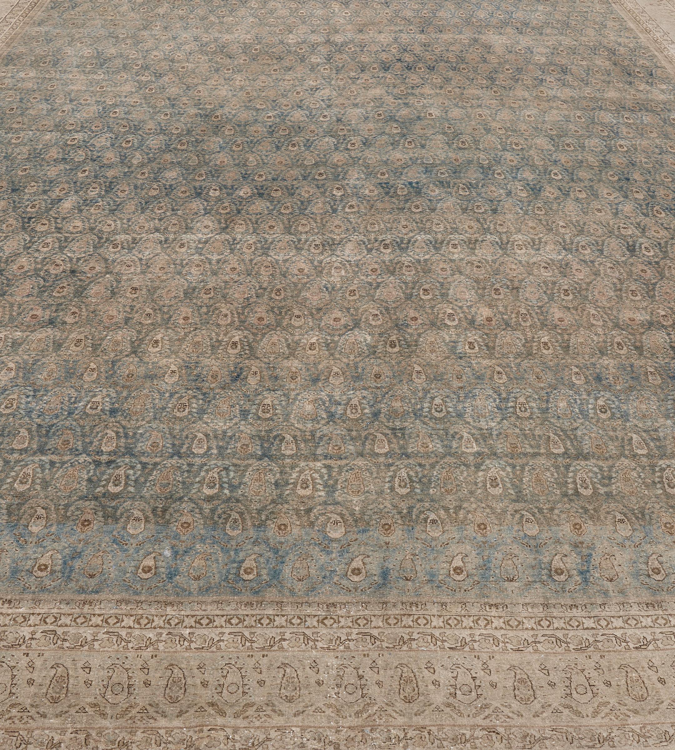 Dieser antike, um 1900 entstandene persische Täbriz-Teppich hat ein schattiertes blaues Feld mit einem Gesamtmuster aus diagonalen Reihen von buff-braunem und elfenbeinfarbenem boteh, in einer elfenbeinfarbenen Bordüre aus elfenbeinfarbenem boteh,