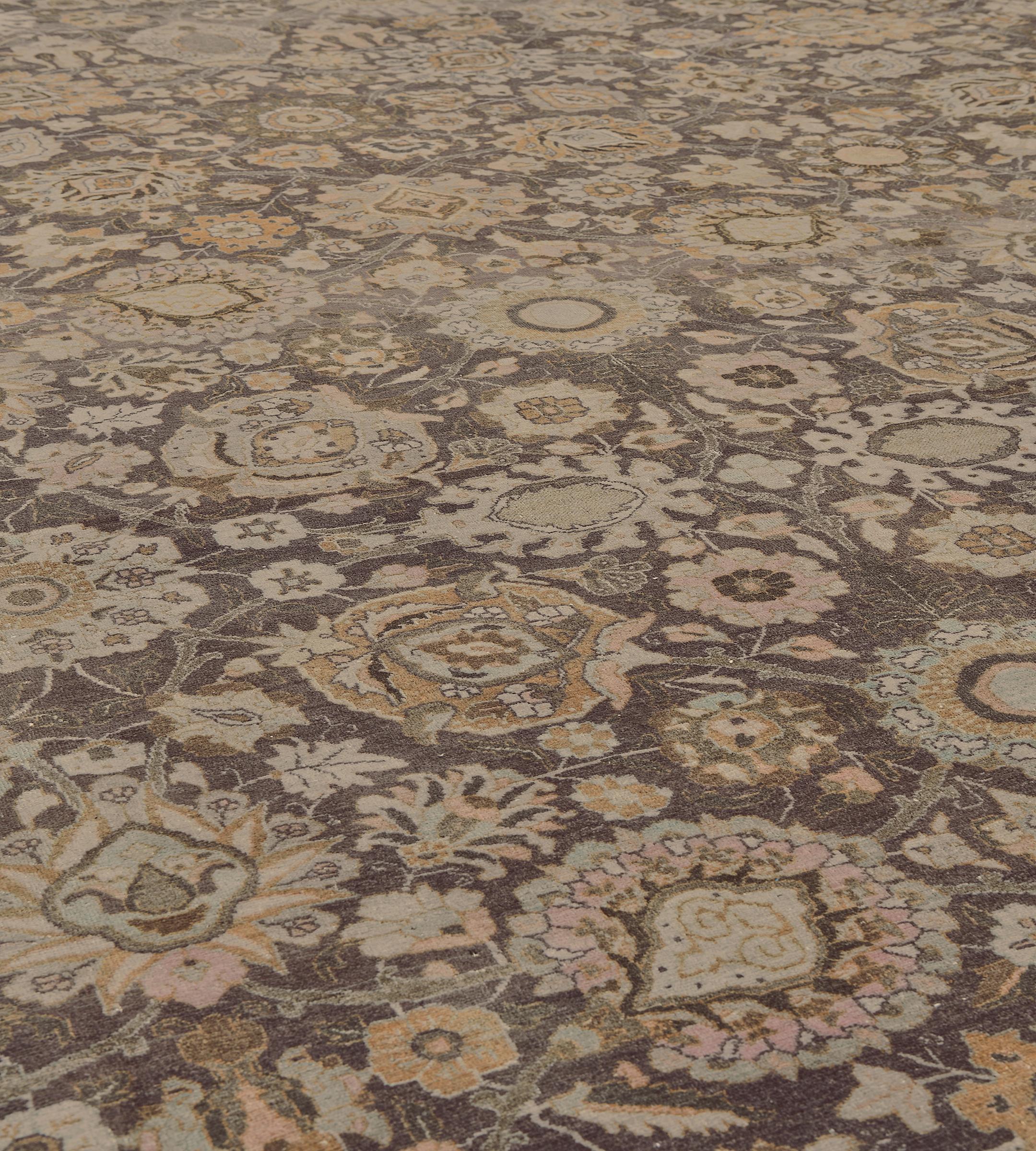 Cet ancien tapis persan Tabriz, datant d'environ 1900, présente un doux champ aubergine-violet avec un motif général de palmettes denses bleu clair, orange brûlé, ivoire et brun taupe et de délicates vignes feuillues, dans une large bordure orange