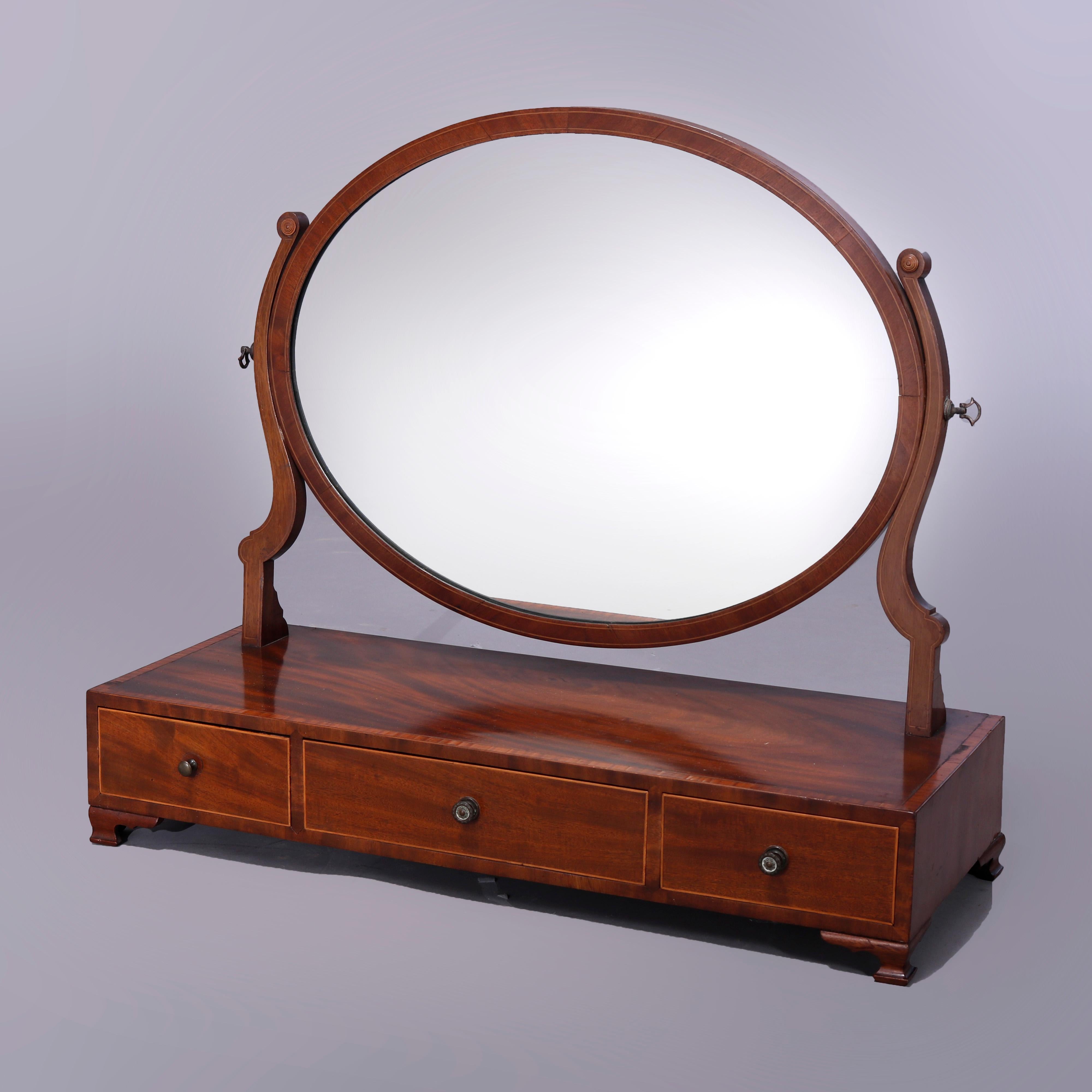 An oversized antique Federal table top dressing or shaving mirror offers oval swivel mirror with flanking scroll form supports surmounting triple drawer cross banded case having satinwood banding and raised on bracket feet, c1830

Measures - 25''H x