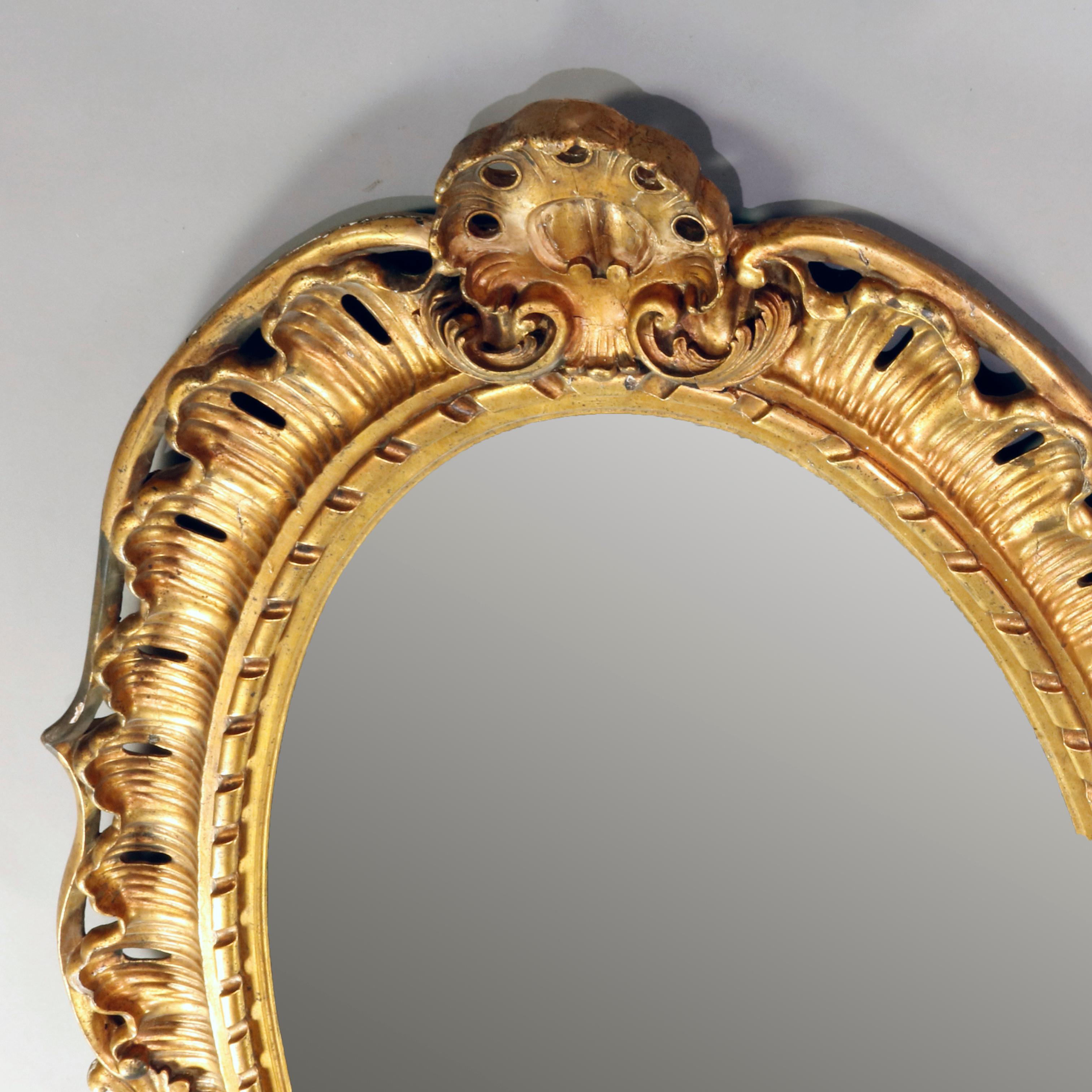An oversized antique French Louis XIV over mantel mirror offers oval form having carved giltwood pierced foliate and scroll bordering with shells at crest and base, 19th century
 

Measures: 78