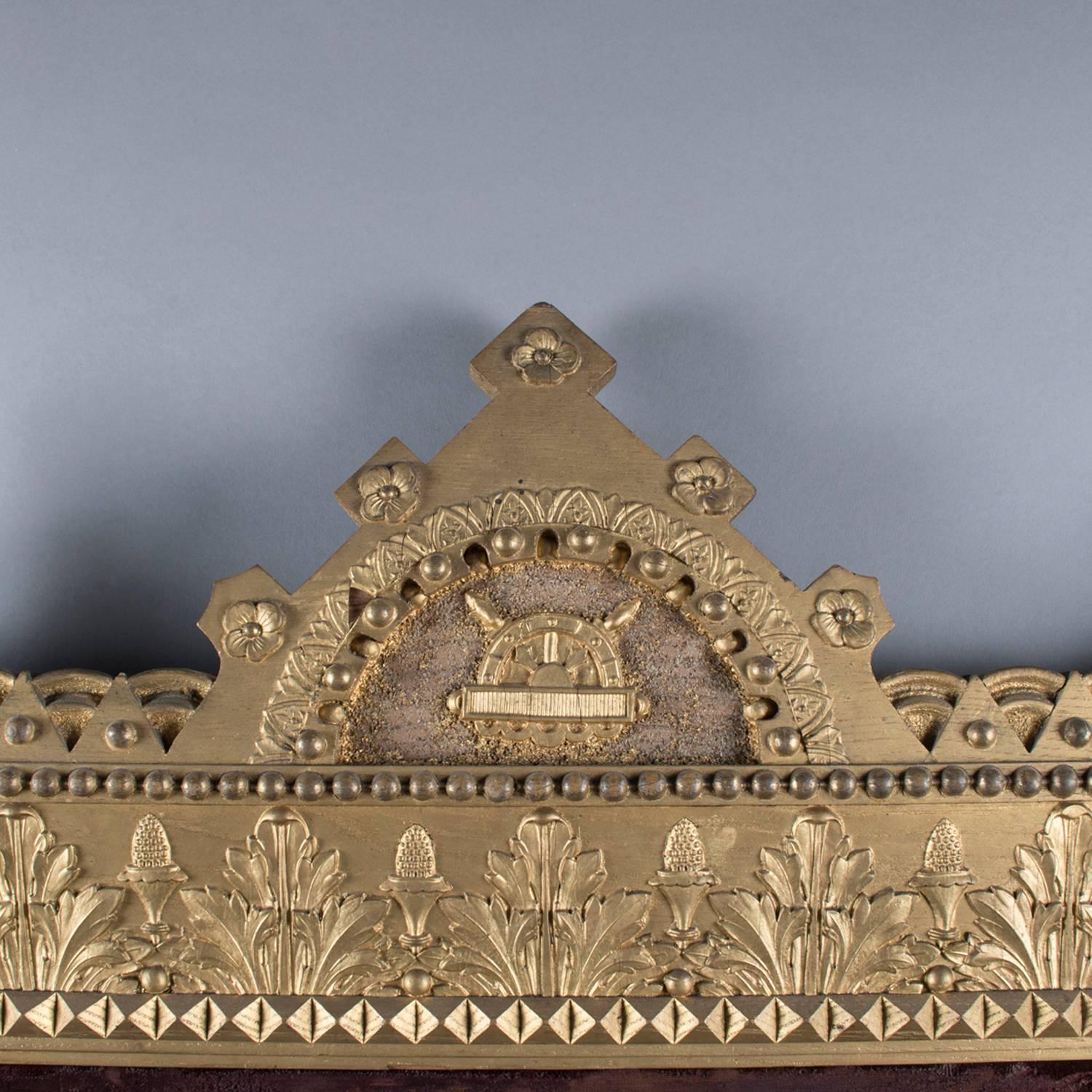 Oversized antique Moorish regal carved giltwood over mantel wall mirror features crown form crest with flanking finials and decorated columns, frame with allover panels of floral and foliate decoration, open dental molding form skirt, 19th