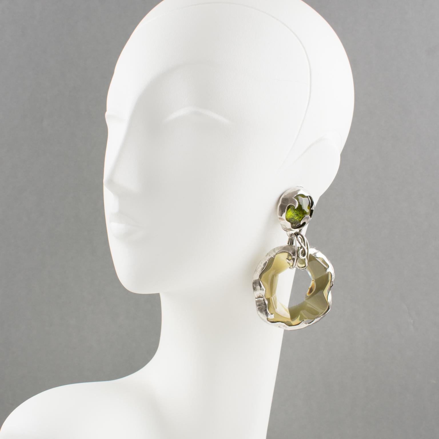 Stunning oversized dangling clip-on earrings. Brutalist design with chandelier shape, featuring a large dangle donut with silverplate metal carved frame compliment with transparent olive green Lucite carved insert element. No visible maker's