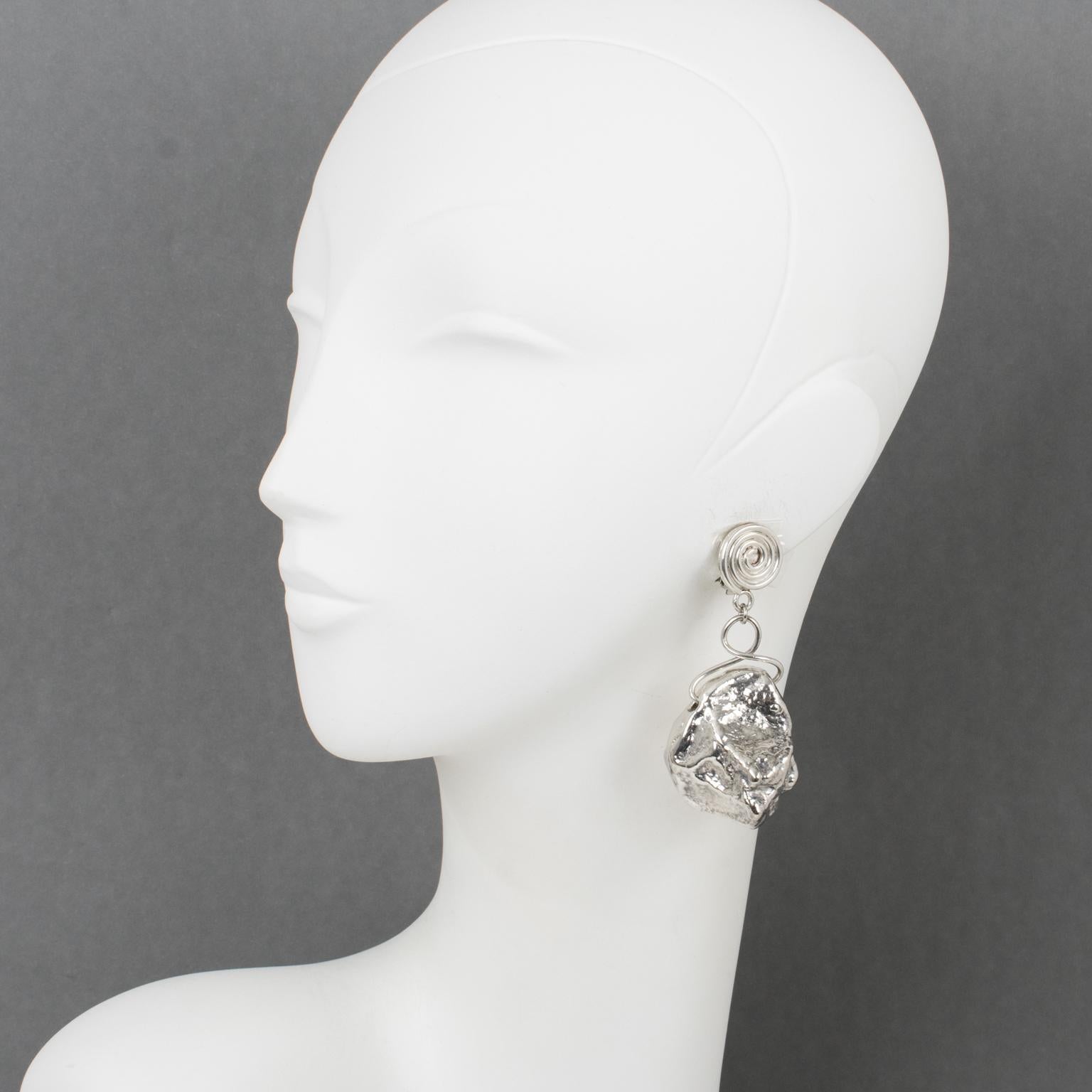 These stunning dangling clip-on earrings feature a brutalist design with an oversized nugget-shaped drop in silver plate metal. The fastening elements have a silver plate spiral design. There is no visible maker's mark.
Measurements: 1.38 in wide