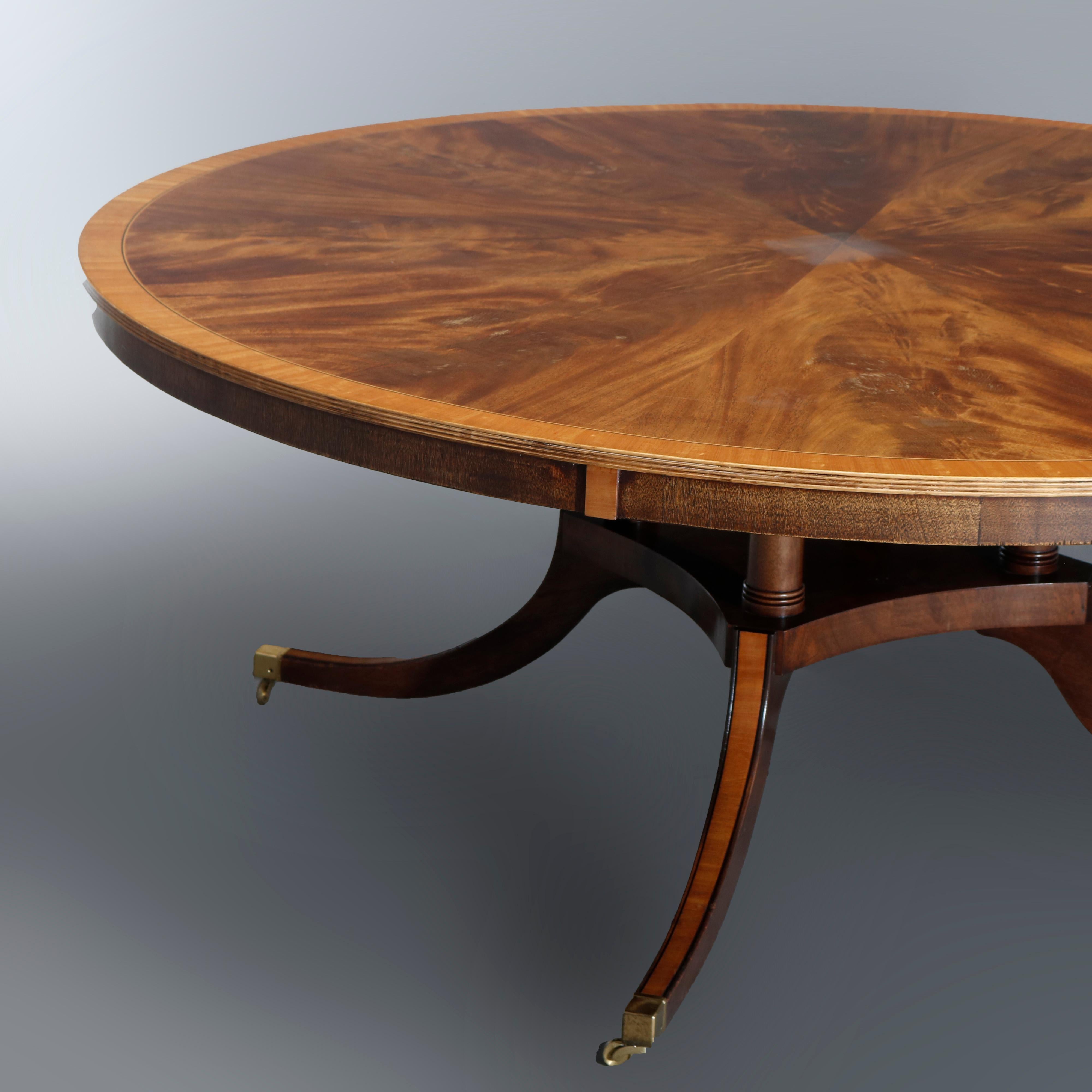 A vintage and oversized Federal style dining or conference table by Rist offers oversized round top with inlaid flame mahogany sunburst having satinwood crossbanding surmounting quadruped birdcage base with inlaid and banded convex bowed legs