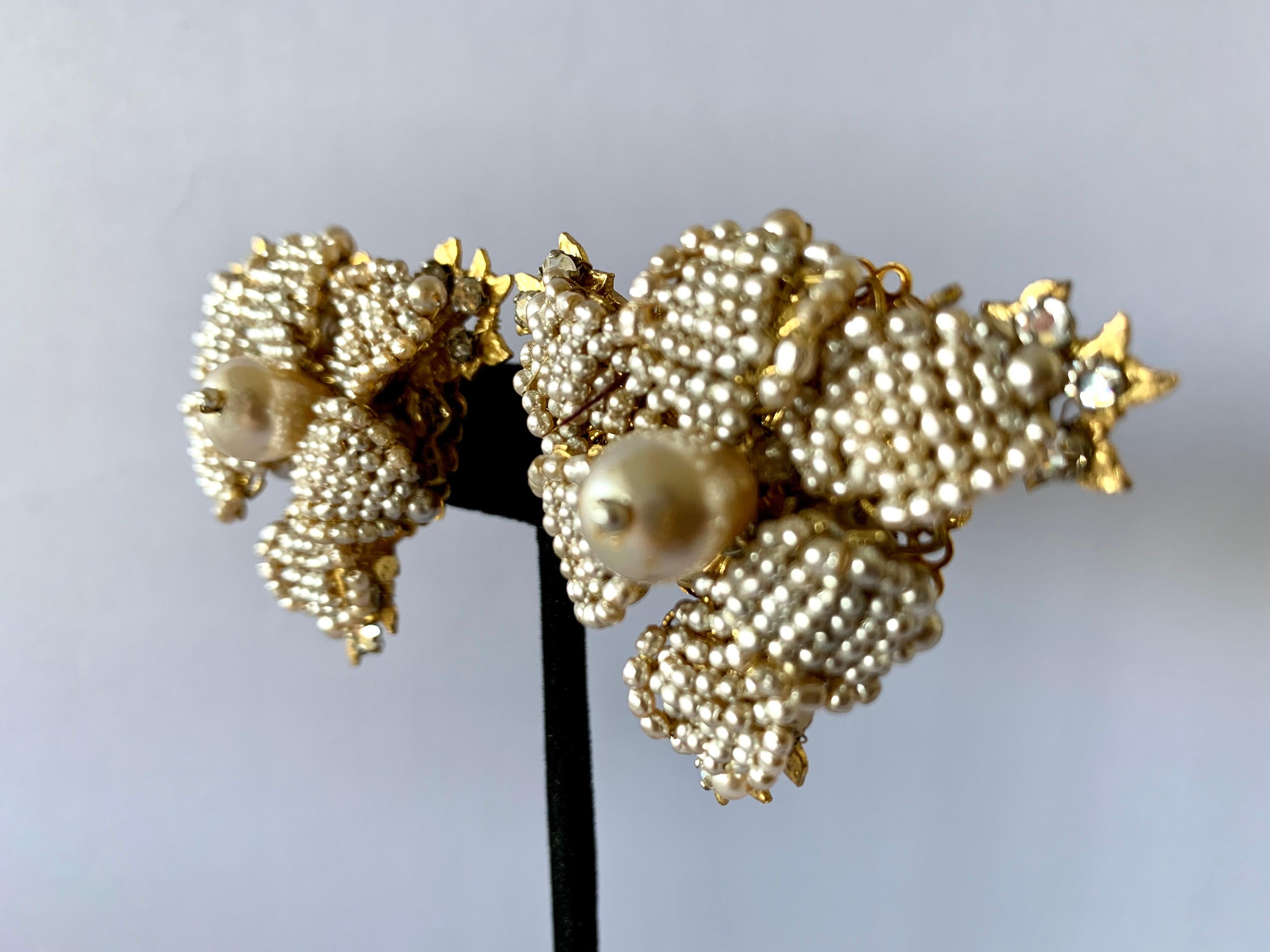 Vintage oversized clip-on earrings comprised out-of gilt metal, intricately beaded with small pearls and diamante rhinestones depicting detailed flowers. The earrings were created by William de Lillo and Robert F. Clark circa 1979/80, signed delillo.