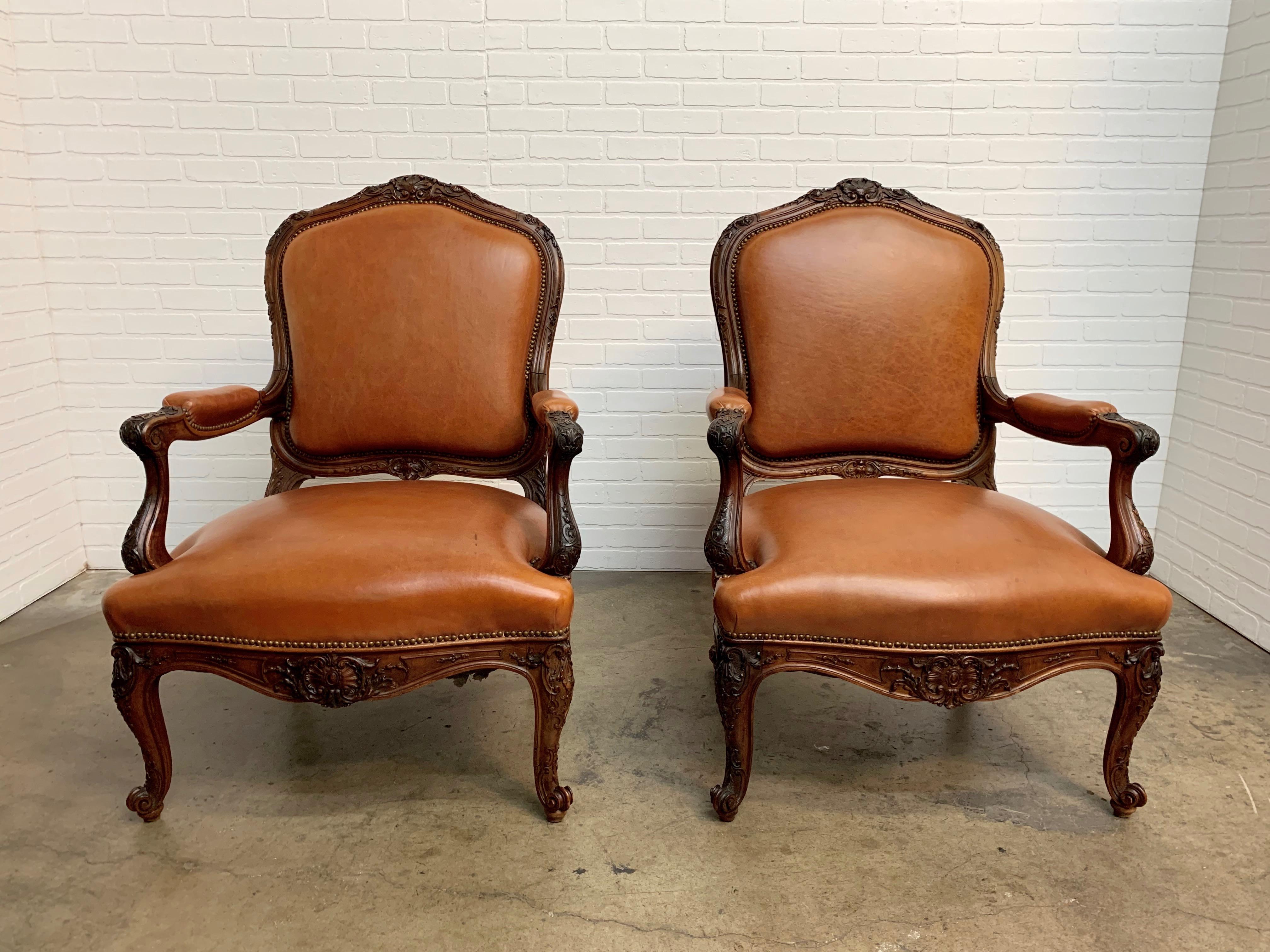 Pair of antique Louis XV style solid walnut throne lounge chairs with leather upholstery and brass nailheads.